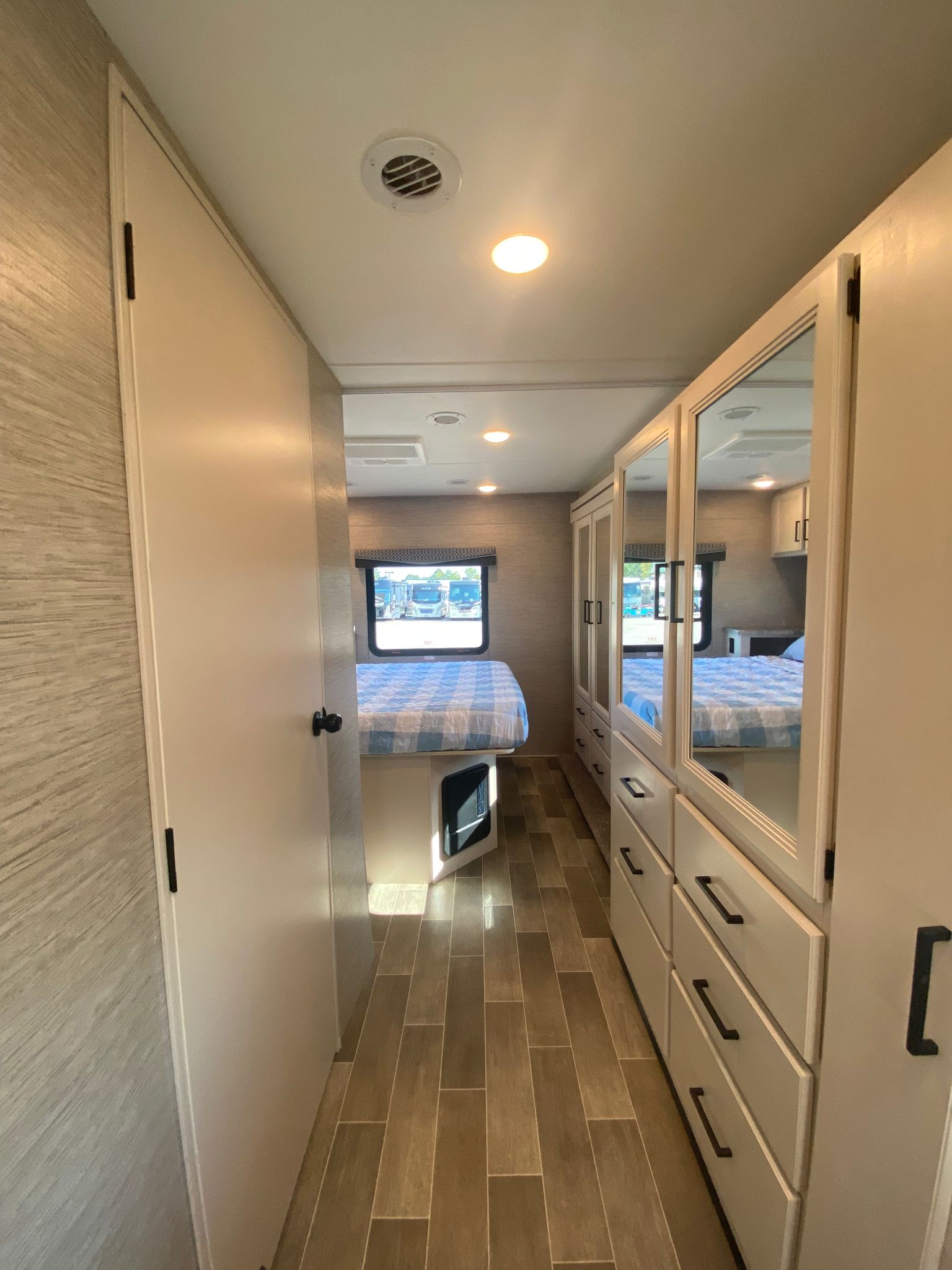 RV rental interior: A bright hallway leads to a bedroom with a checkered bed, featuring mirrored closets and wood-look floors.. Thor Motor Coach Chateau 2022