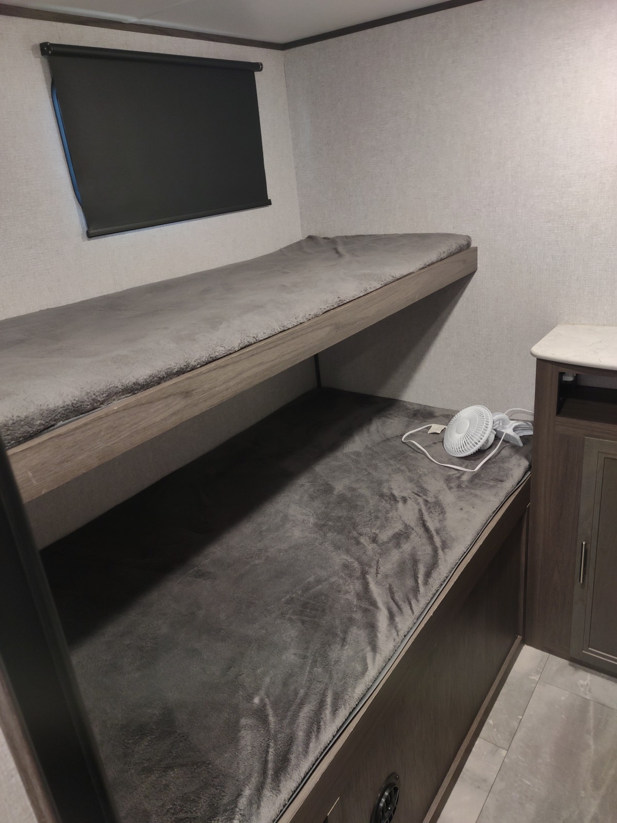 RV rental: Two cozy bunk beds with grey bedding, a window blind, and a white clip-on fan, ideal for comfort.. Dutchmen Kodiak SE 2021