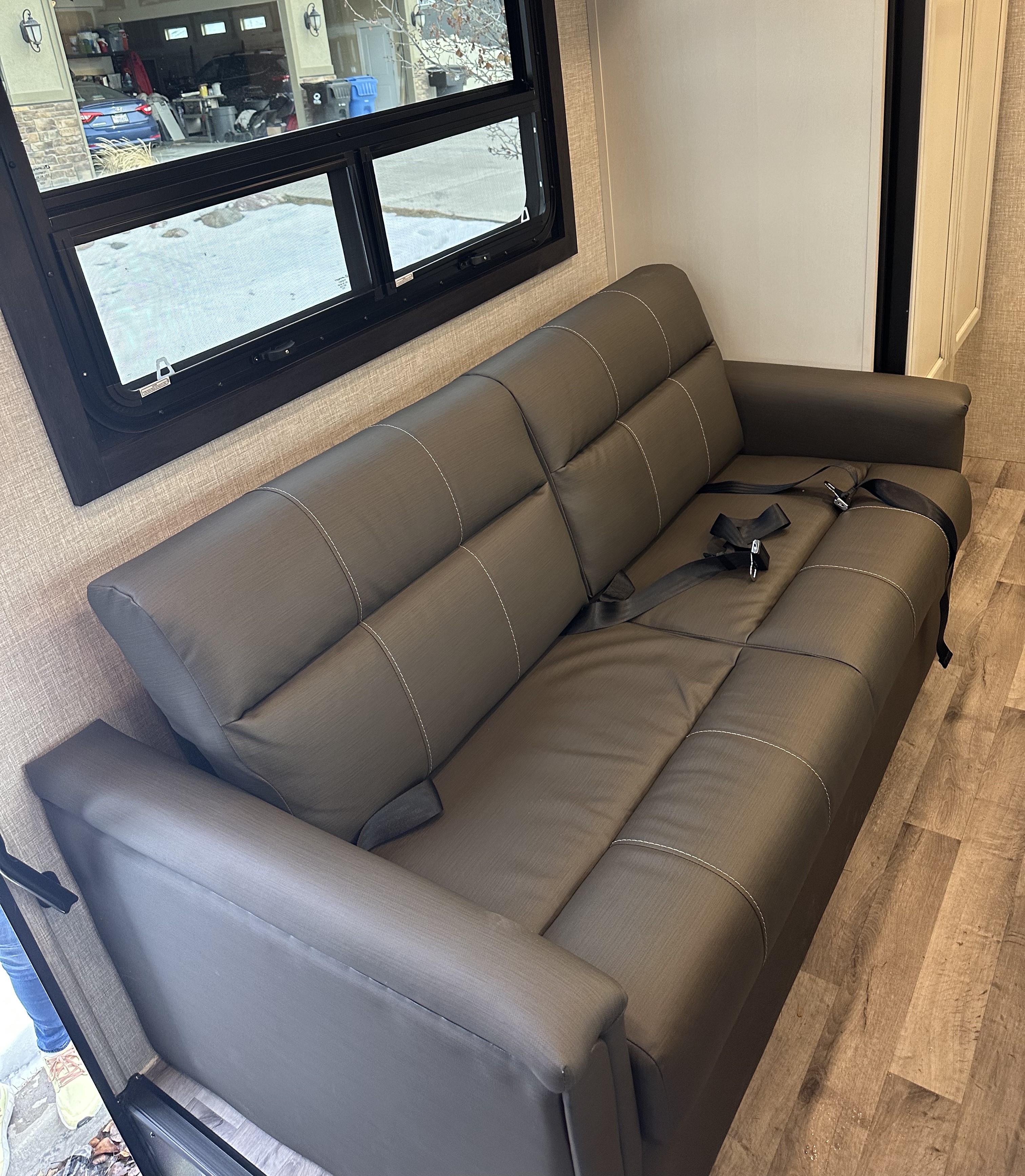 A dark gray RV sofa with white accent stitching and black seatbelts, typical of an RV rental interior, offering comfortable seating.. Jayco Greyhawk 2023