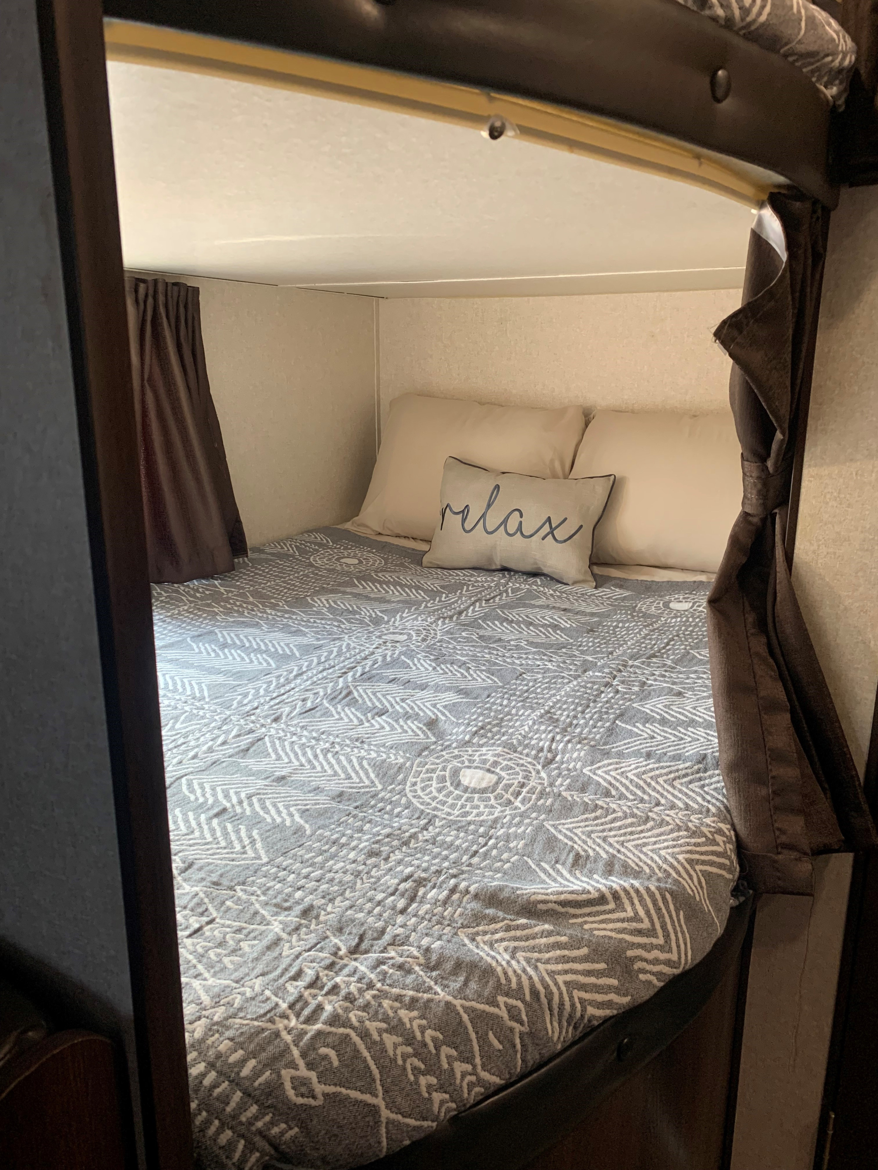 This cozy RV rental sleeping area features a comfy bed with patterned quilt, "relax" pillow, and privacy curtains.. Jayco Jay Flight SLX 2018