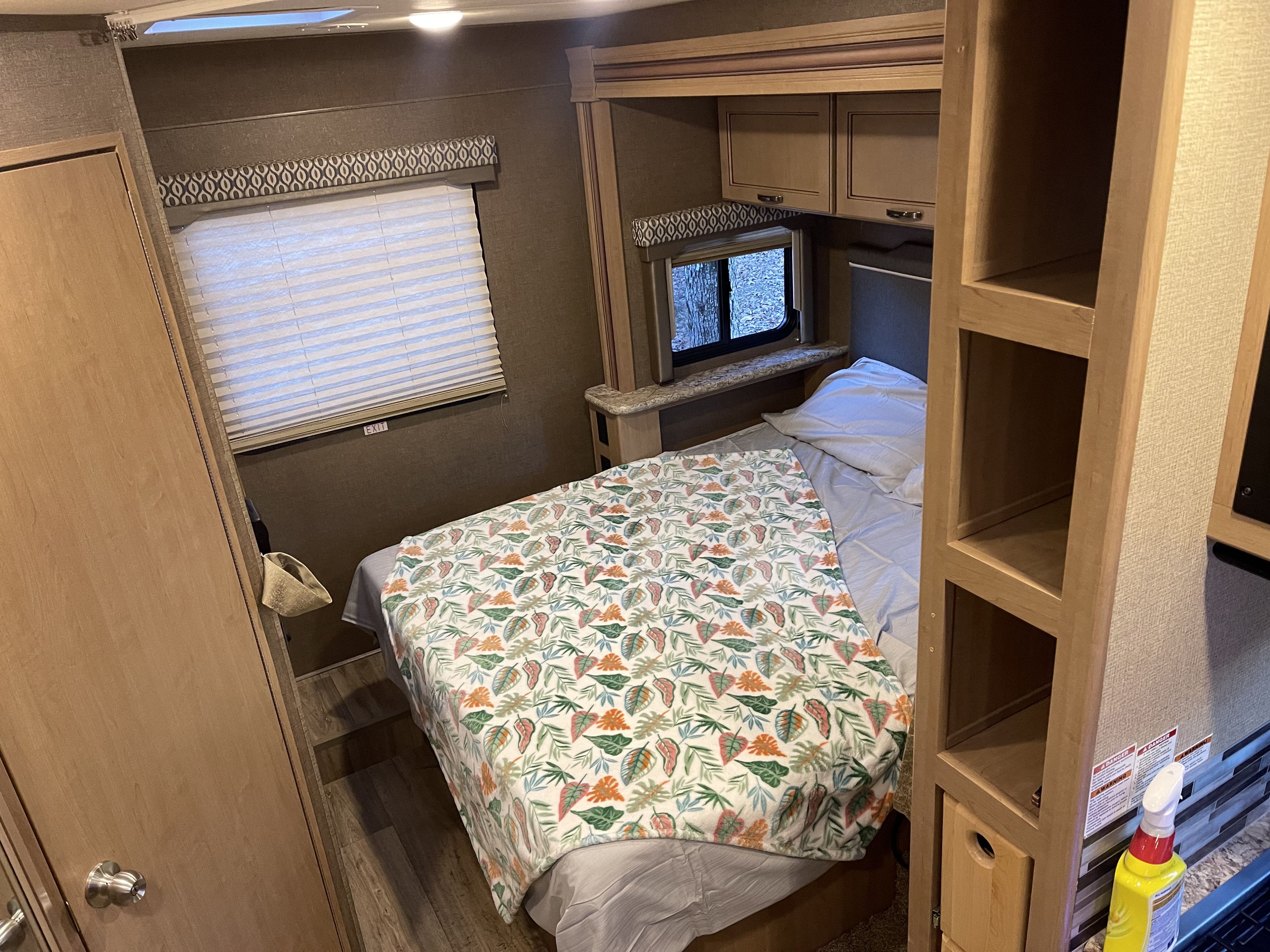Inside an RV rental: cozy bedroom with leaf-patterned blanket, window, and cabinetry. Ready for adventure!. Thor Freedom Elite 2019