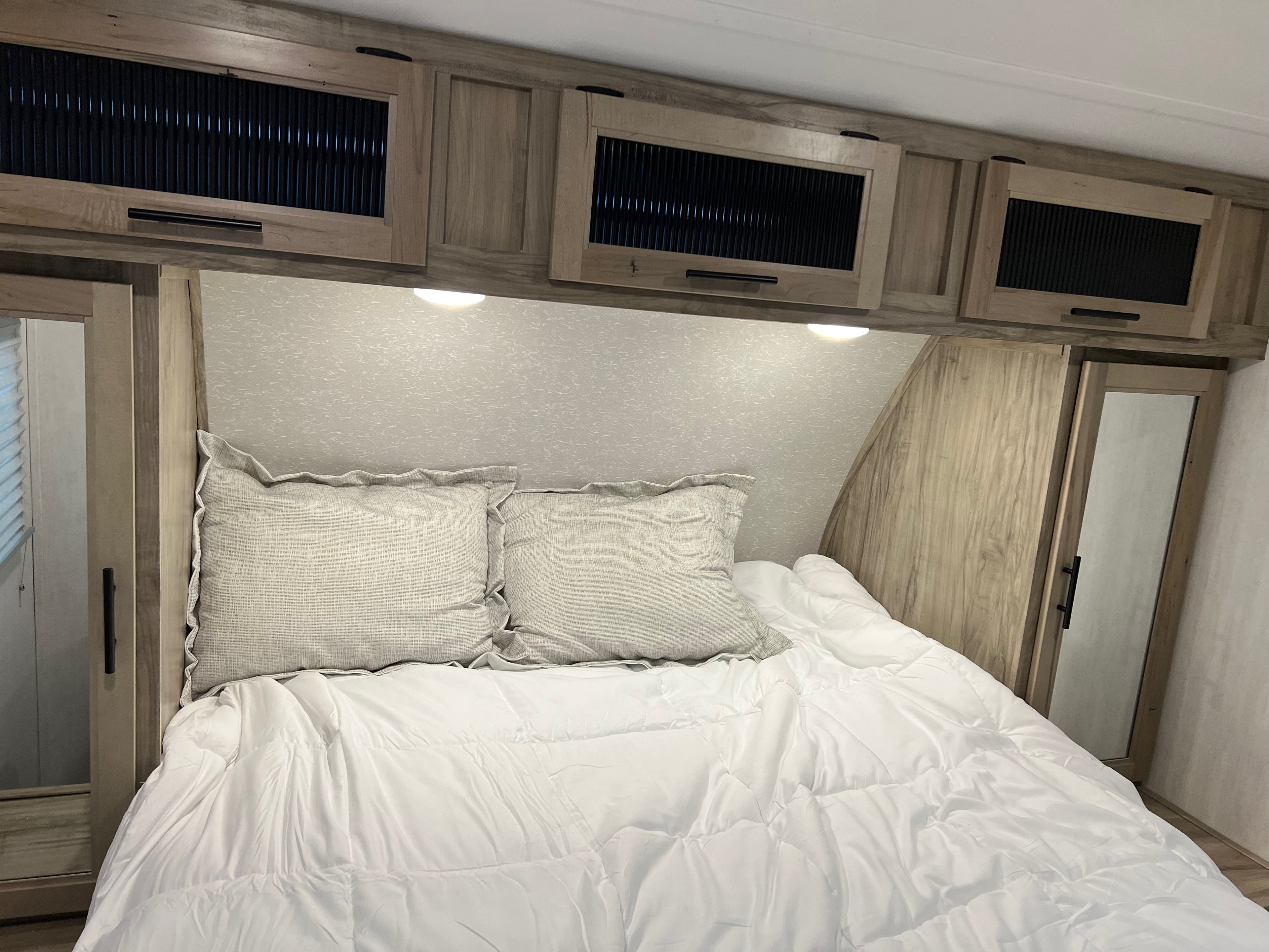Relax in this cozy RV rental bedroom featuring a comfy bed, ample overhead storage with modern accents, and soft lighting.. Forest River Cherokee 2022