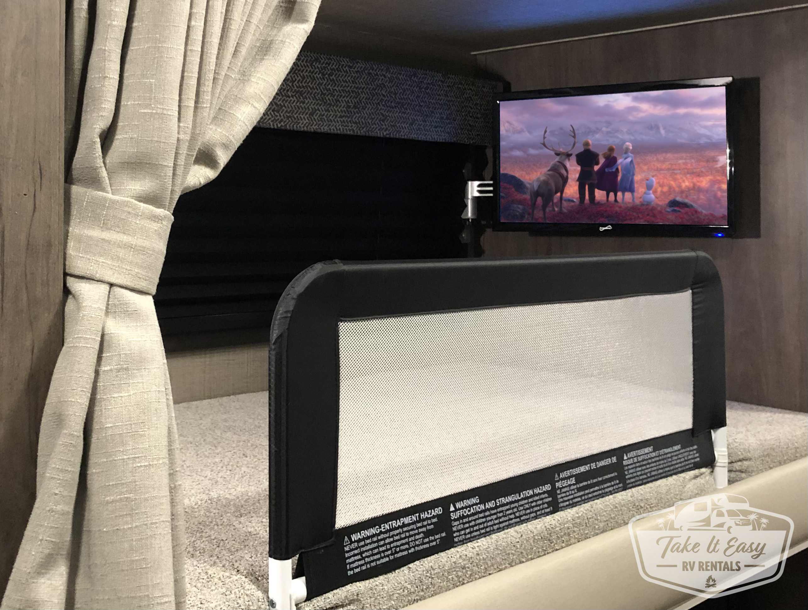 Cozy RV rental bunk with safety rail & TV playing Frozen. Ideal for family travel, ensuring comfort and safety onboard.. Jayco Redhawk 2023