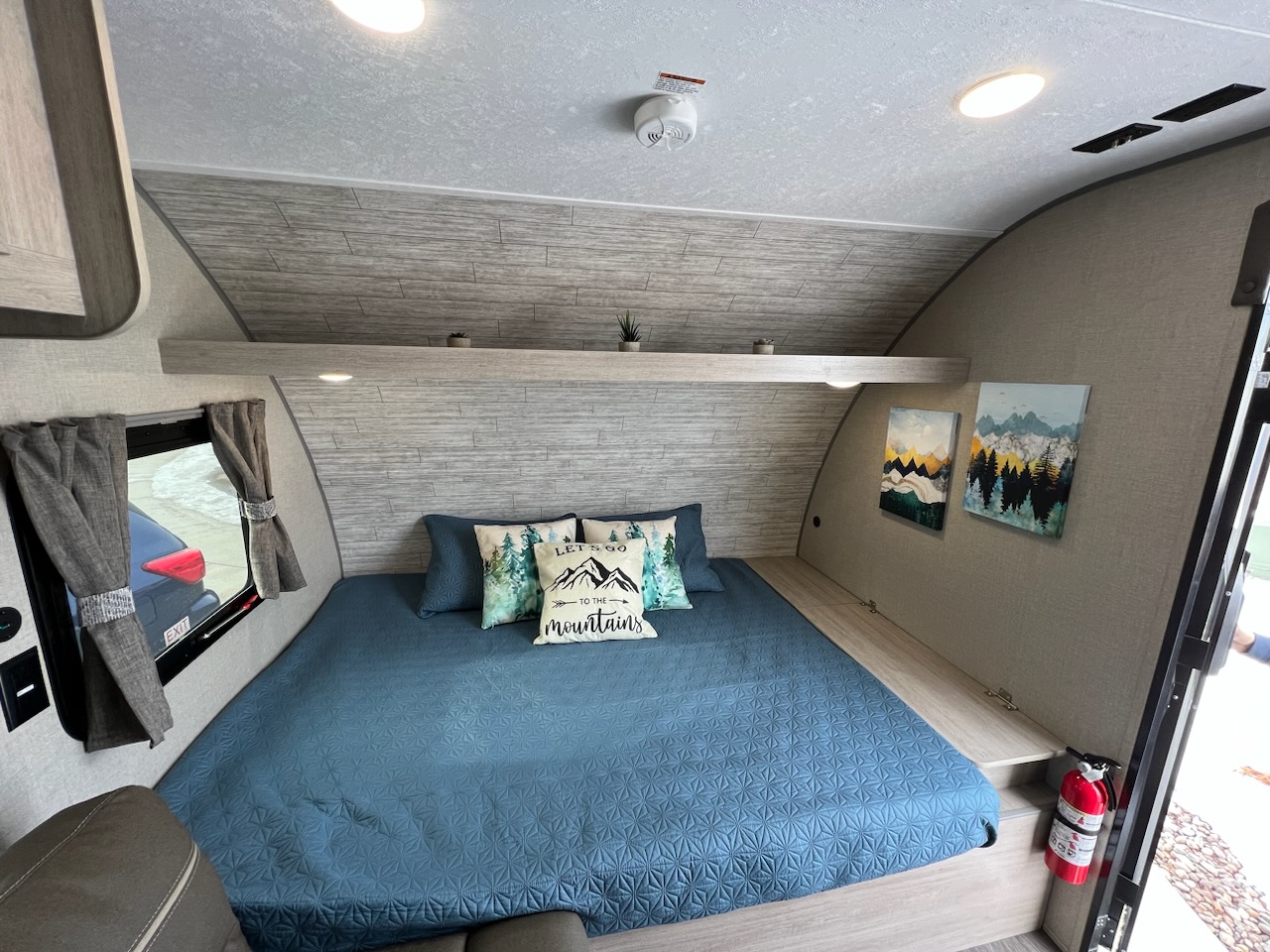 Cozy RV rental bedroom featuring a blue bed, mountain-themed pillows, and wall art. Perfect for travel.. Forest River AURORA 2023