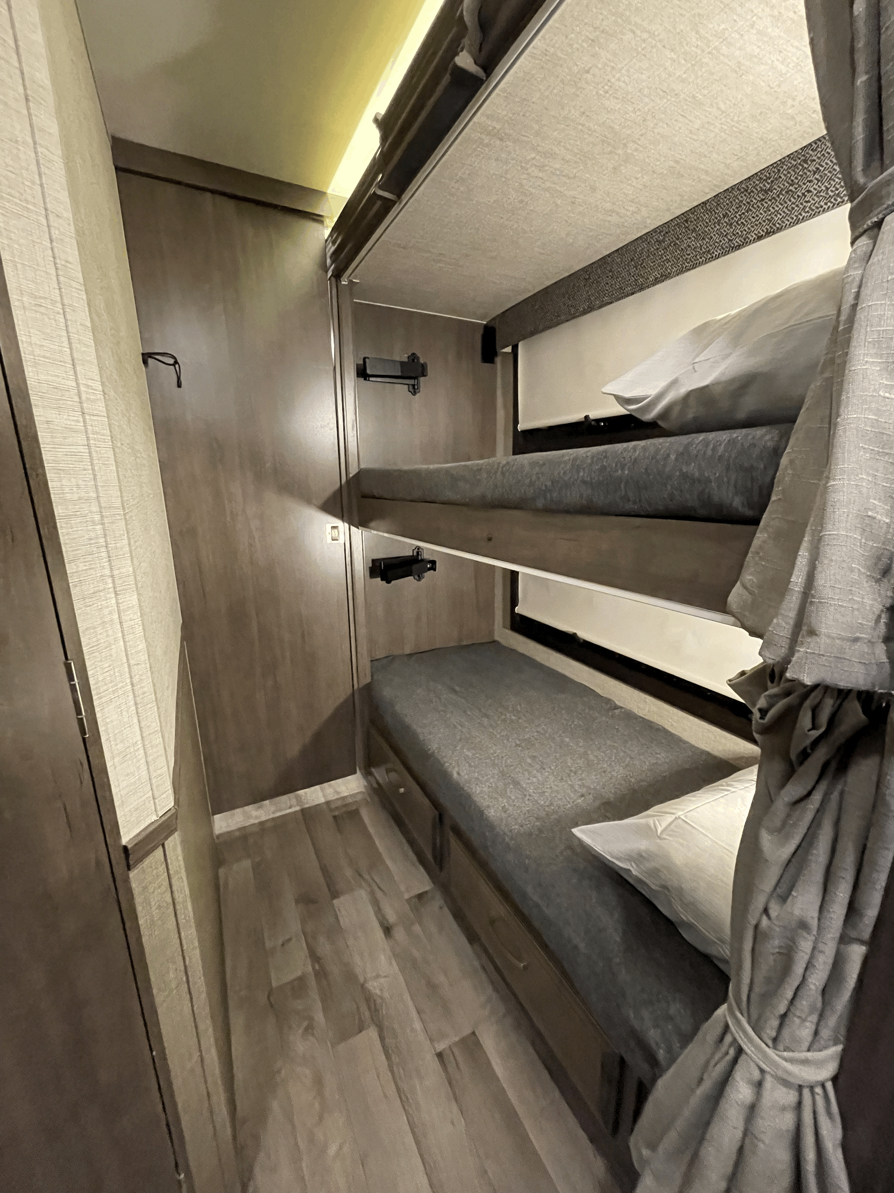 RV rental interior: two-tier bunk beds with grey bedding, privacy curtains, and wall mounts, ideal for families.. Jayco Alante 29F 2023