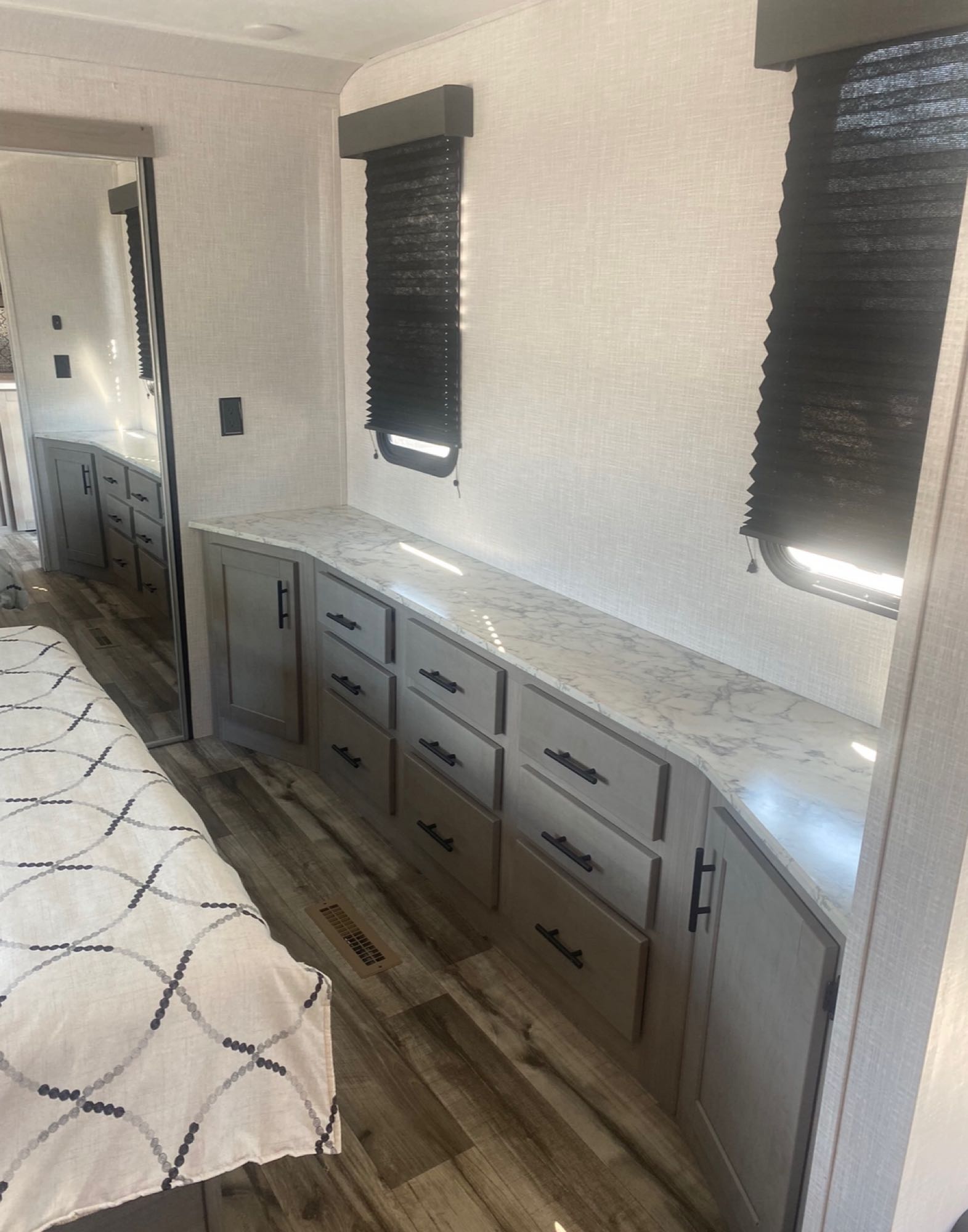 Modern RV rental bedroom with ample storage: a long dresser, two windows with blinds, and a patterned bed on wood-look floor.. Coleman Light 2022