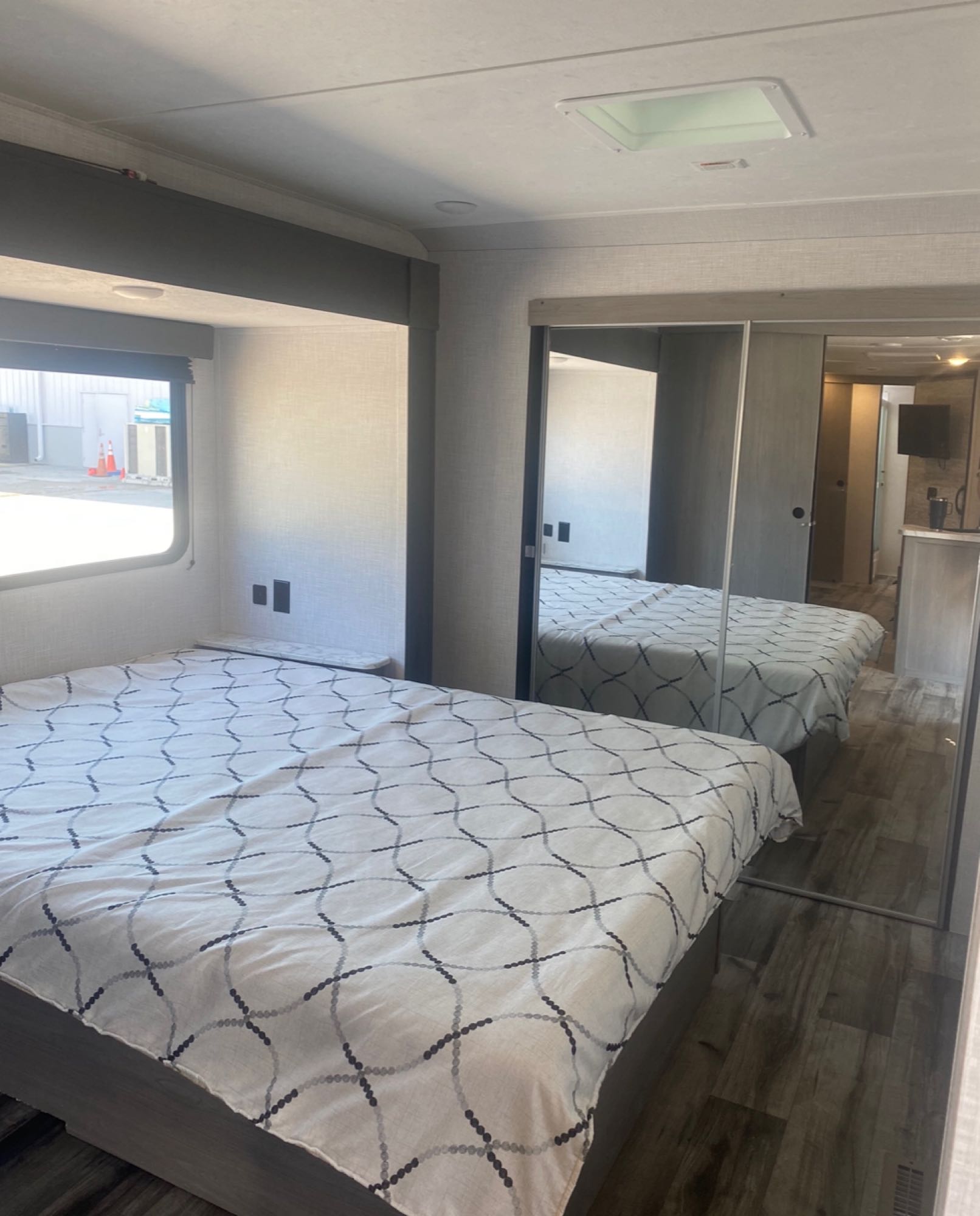 This RV rental bedroom features a patterned bedspread, convenient nightstands, a large window, and mirrored closet doors.. Coleman Light 2022