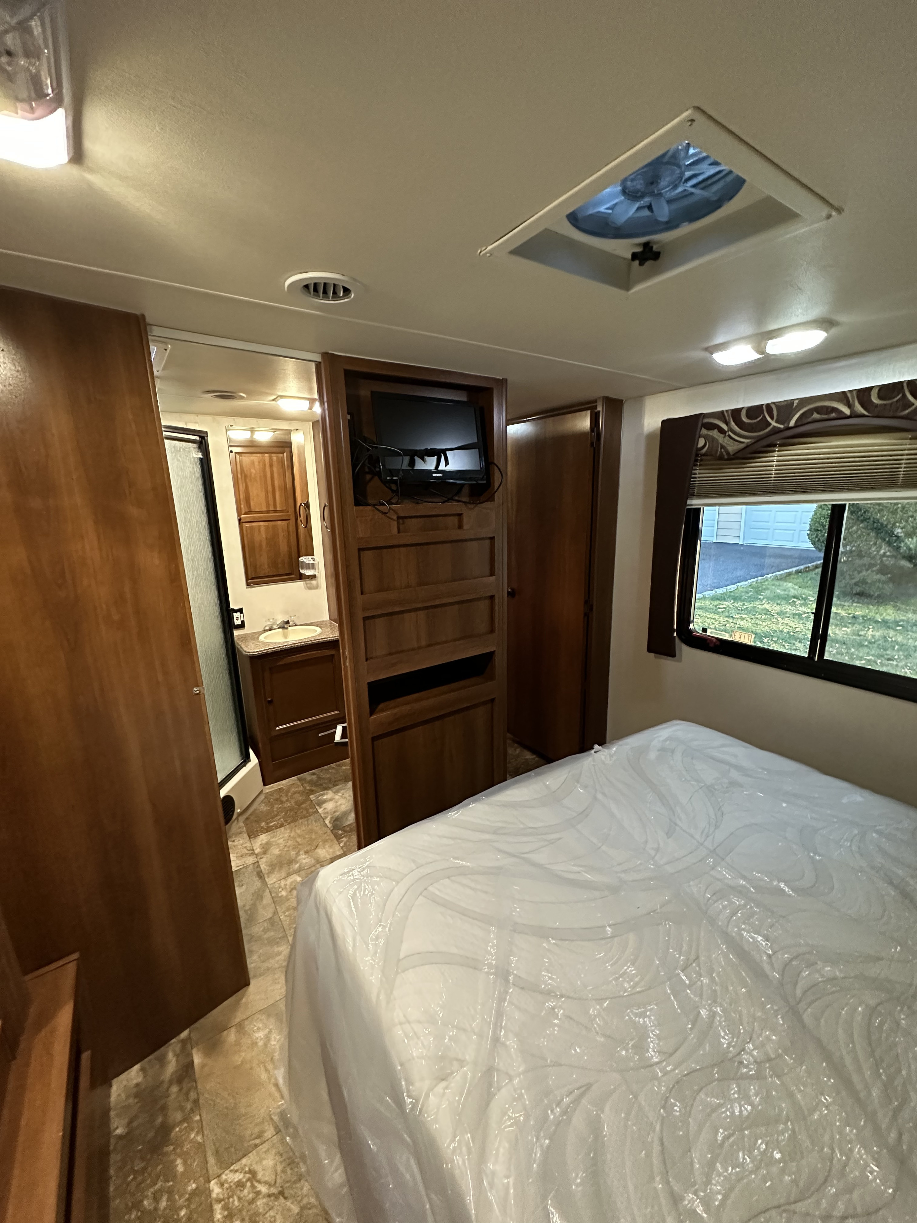 RV rental bedroom with bed (still in plastic), built-in TV, and sliding door to the bathroom.. Forest River Coachmen Leprechaun 2013