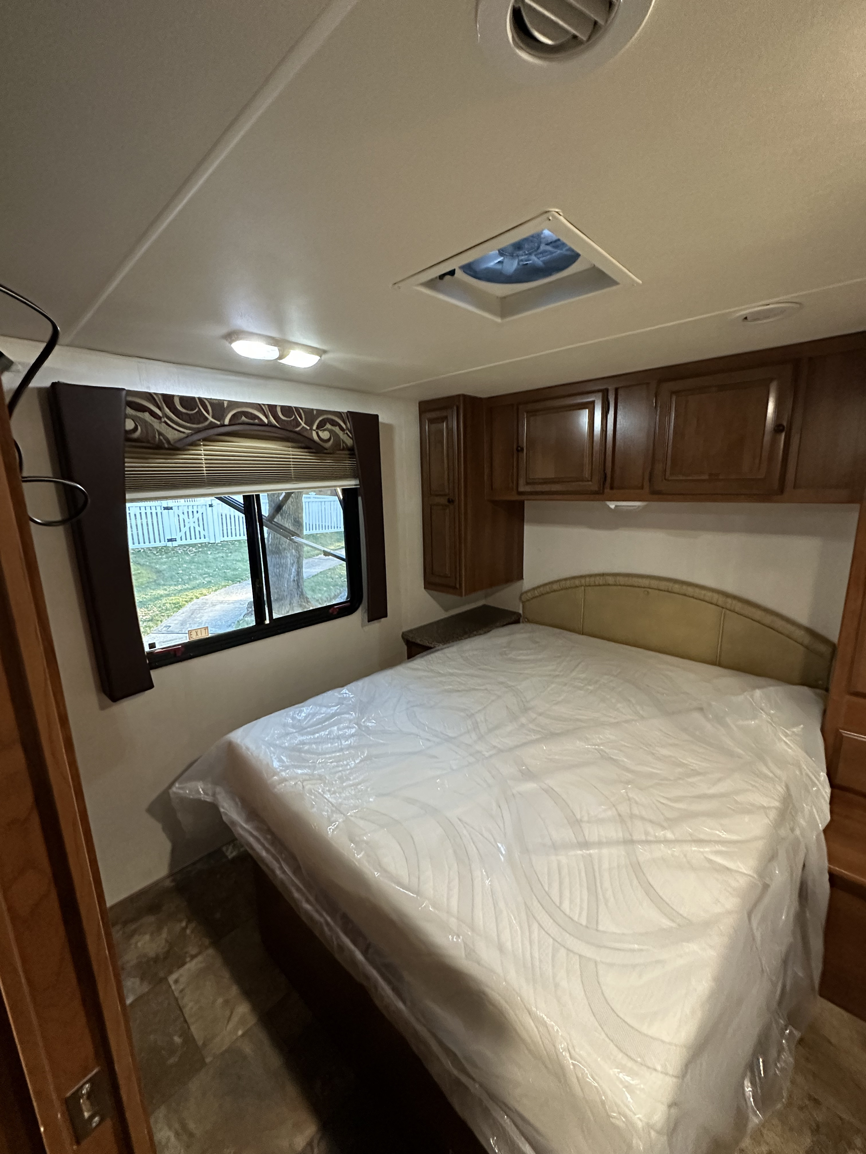 RV rental bedroom featuring a new mattress with protective plastic, wood cabinets, ceiling fan, and window view. Ready for your trip!. Forest River Coachmen Leprechaun 2013