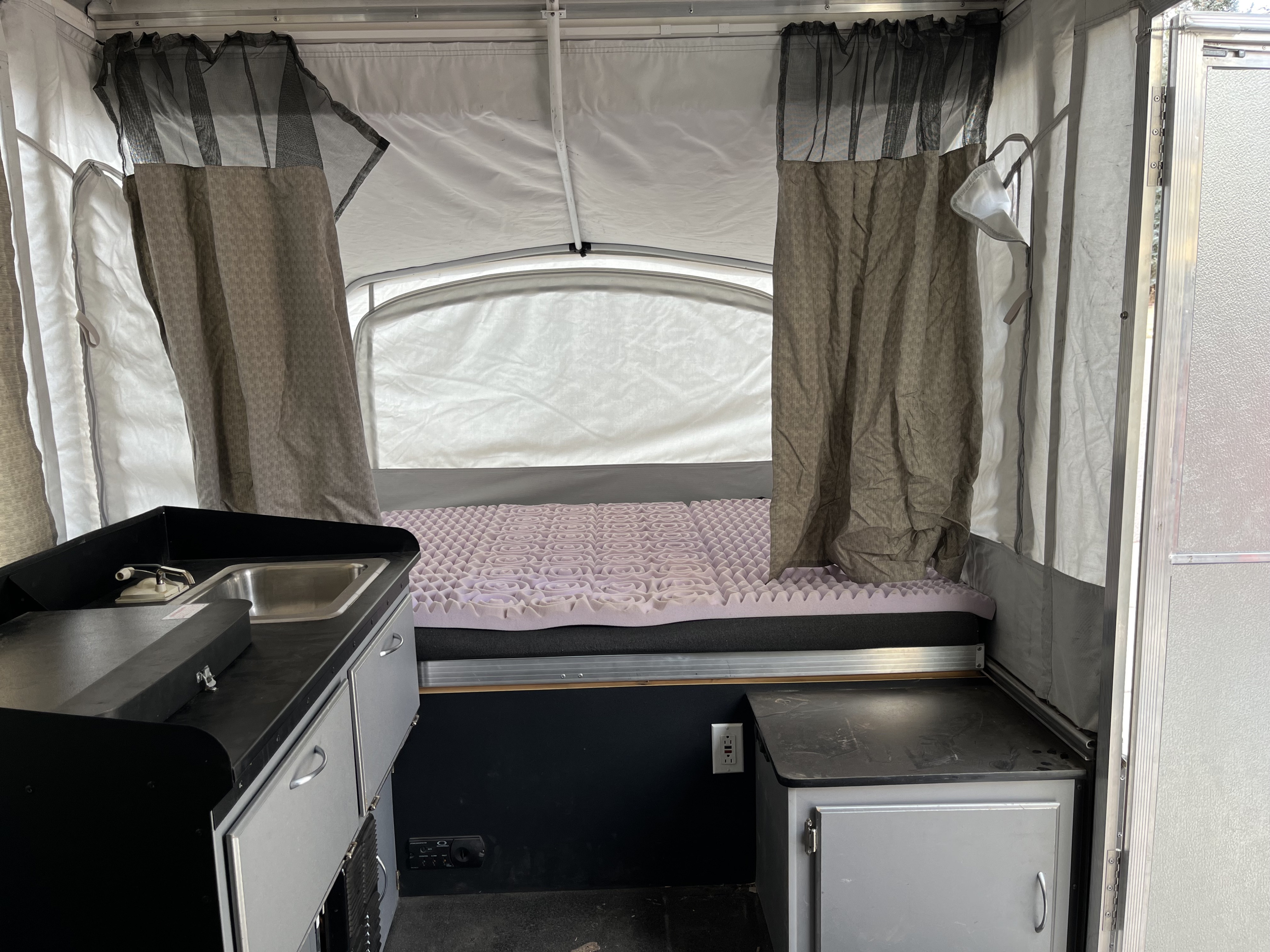 RV rental: Interior of a pop-up camper, showing kitchen sink area, bed with purple topper, and fabric walls.. Fleetwood Cobalt 2008