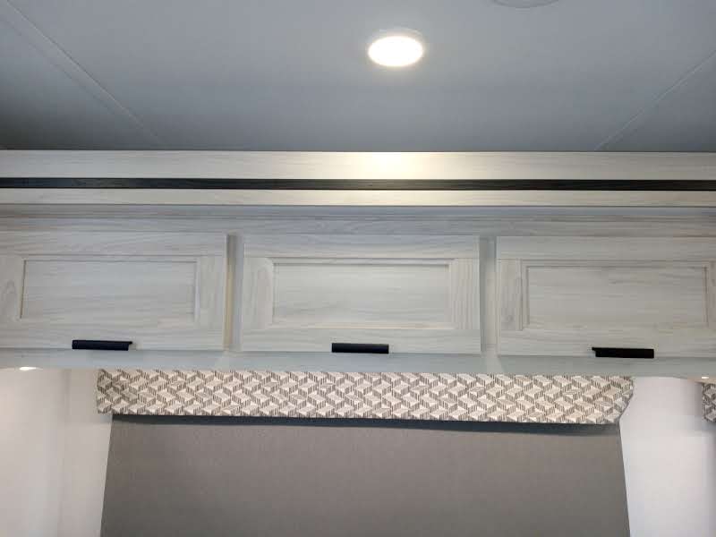 Bright RV rental interior: Overhead light wood cabinets, ceiling light, and patterned valance for essential storage.. Forest River Forester 2024