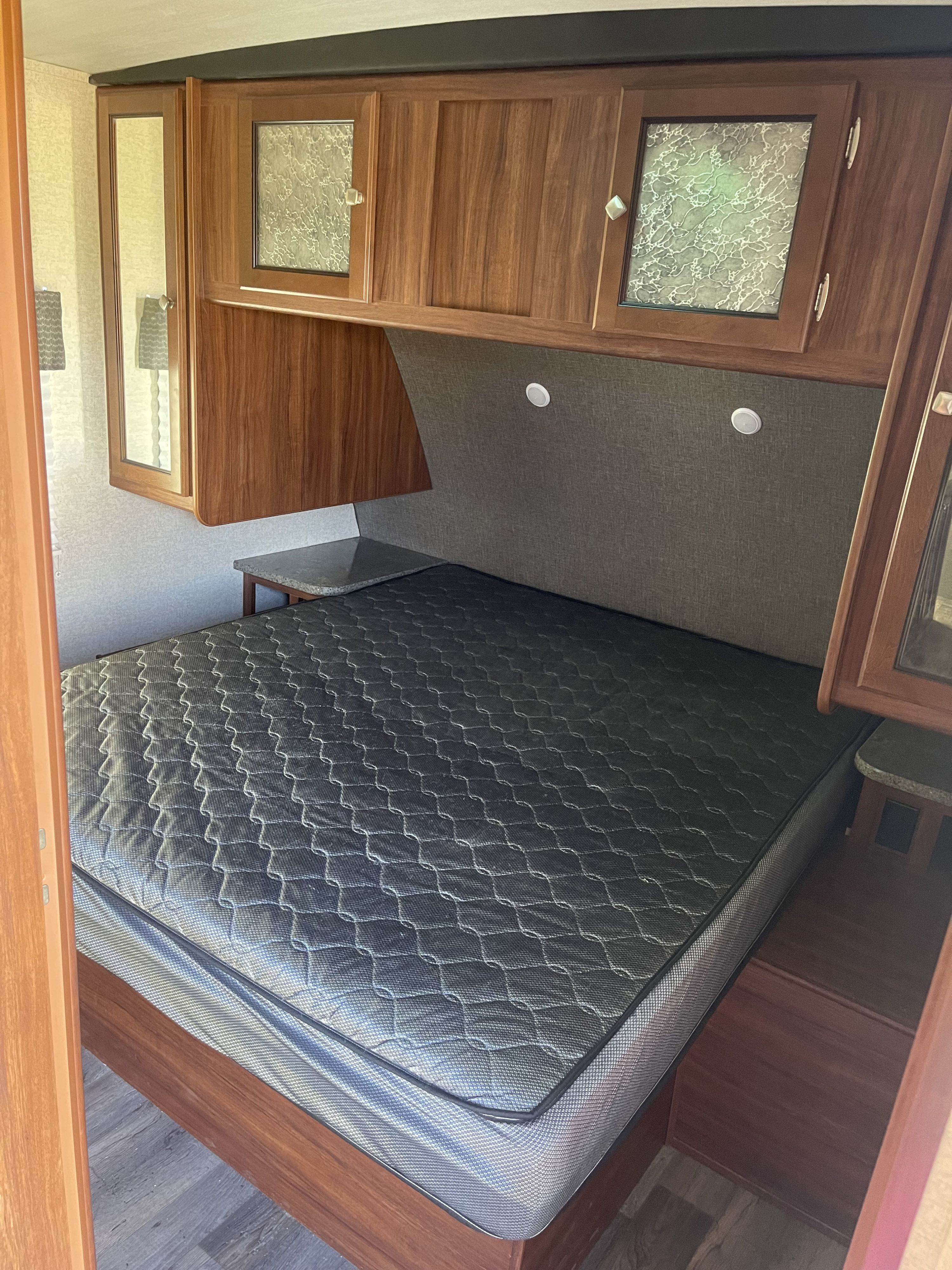 RV rental bedroom with a dark mattress, wooden overhead cabinets with decorative glass, and side tables.. Heartland RVs Mallard 2017