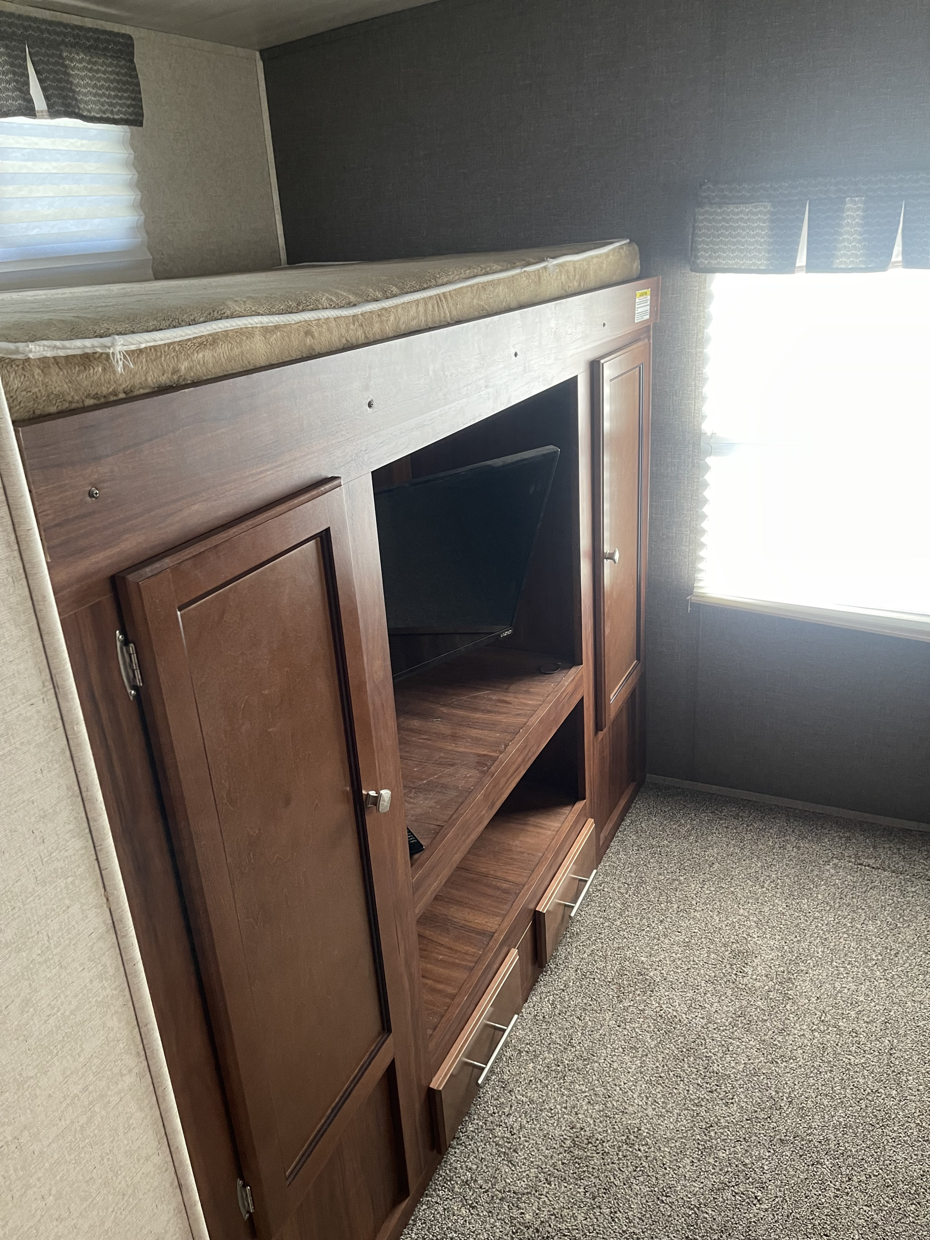 Inside an RV rental: Cozy bunk bed with storage, TV nook, and window. Carpeted floor offers comfort.. Heartland RVs Mallard 2017