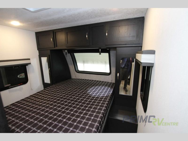 Inside an RV rental: a compact bedroom featuring a bed with checkered bedding, storage cabinets, and windows.. Coachmen Freedom Express 252RBS 2022