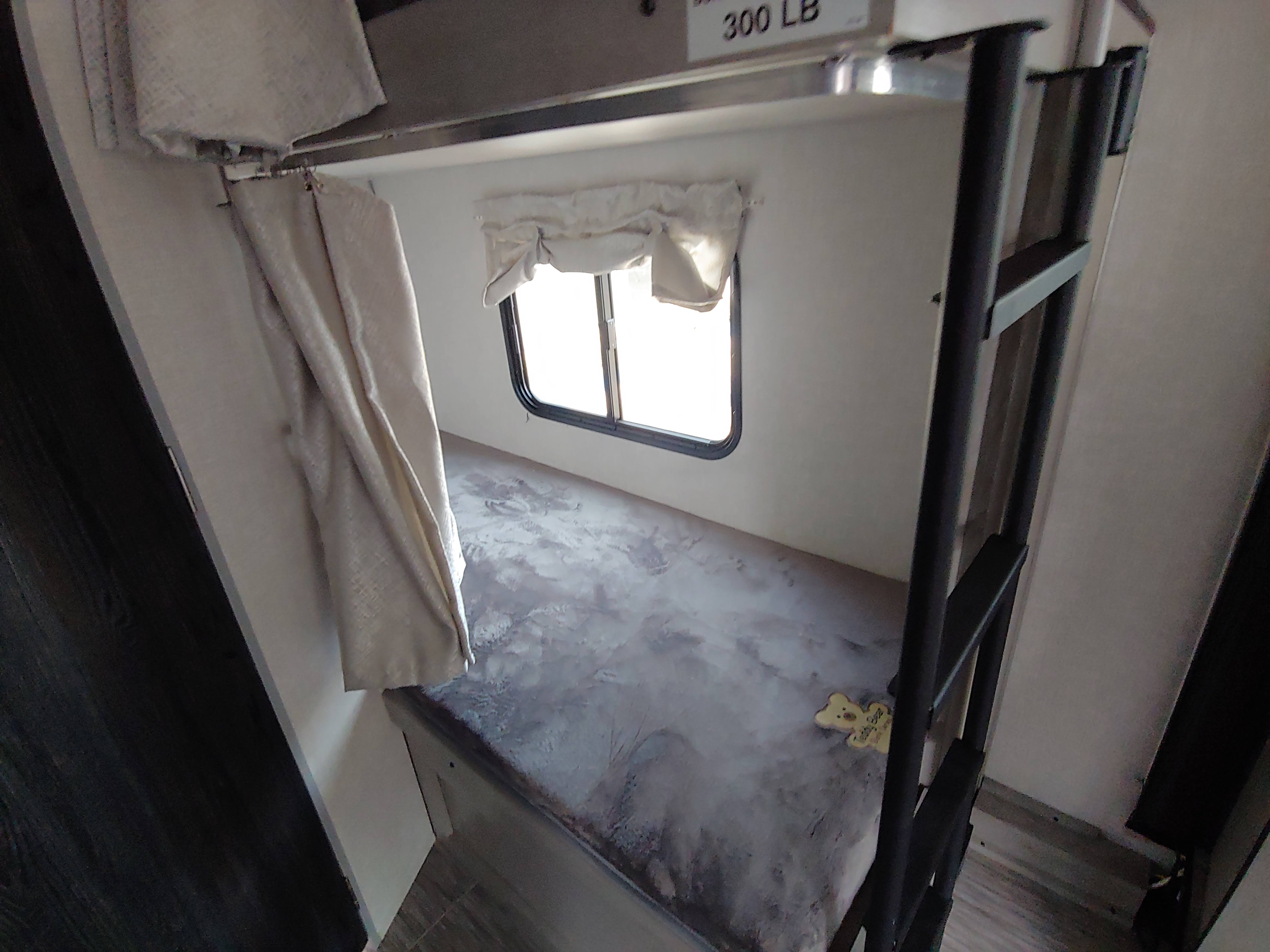 Cozy RV rental bunk bed area with a window, privacy curtain, and an access ladder.. Forest River Ibex 2021