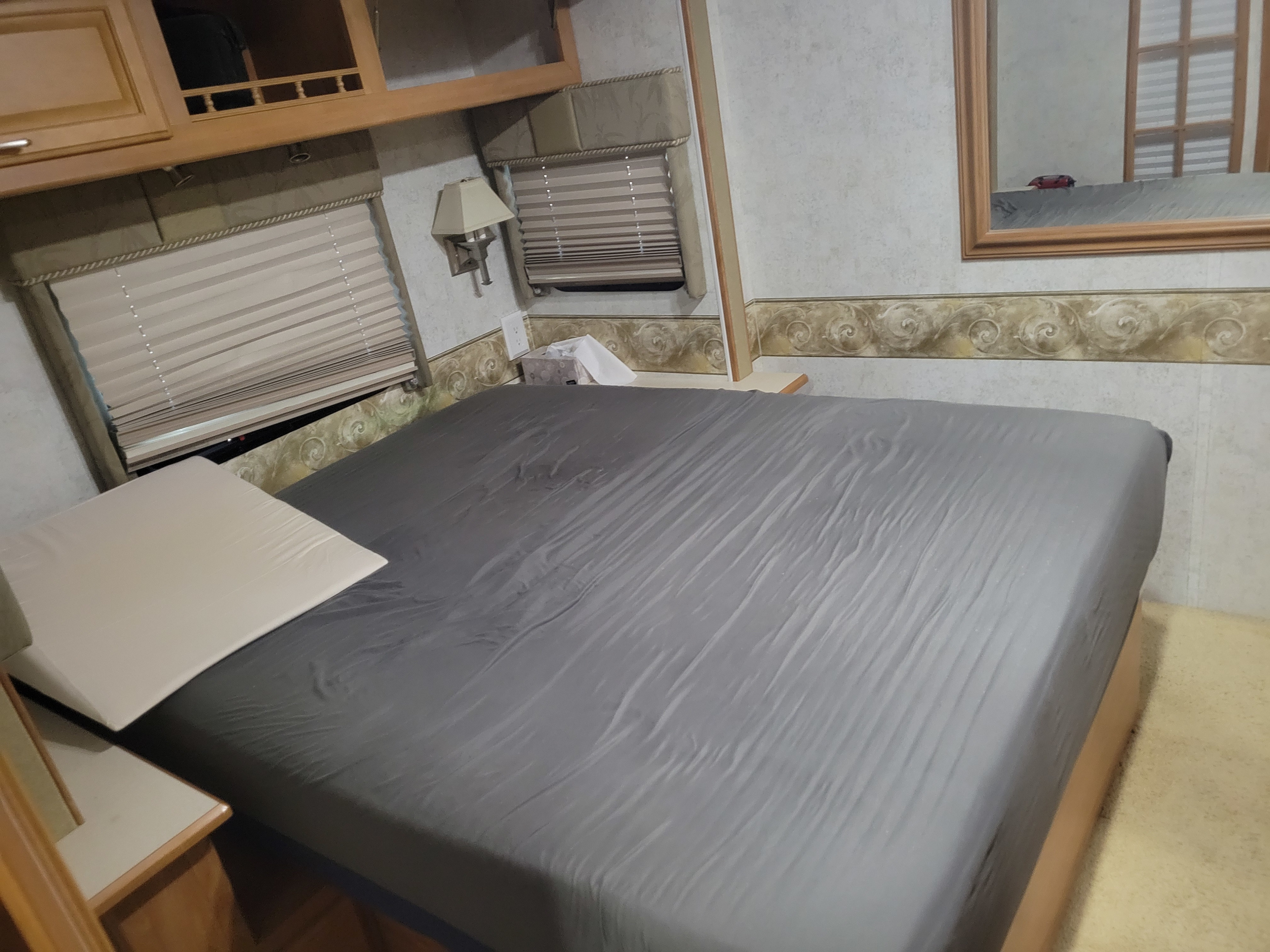 Cozy RV rental bedroom featuring a grey bed, window blinds, and overhead storage.. Winnebago Adventurer 2005