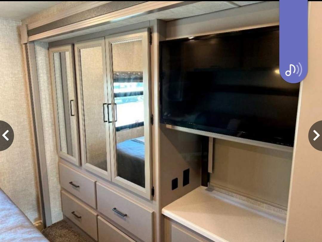 Modern RV rental bedroom with mirrored wardrobe storage, multiple drawers, and a mounted TV entertainment setup.. Thor Windsport 2022