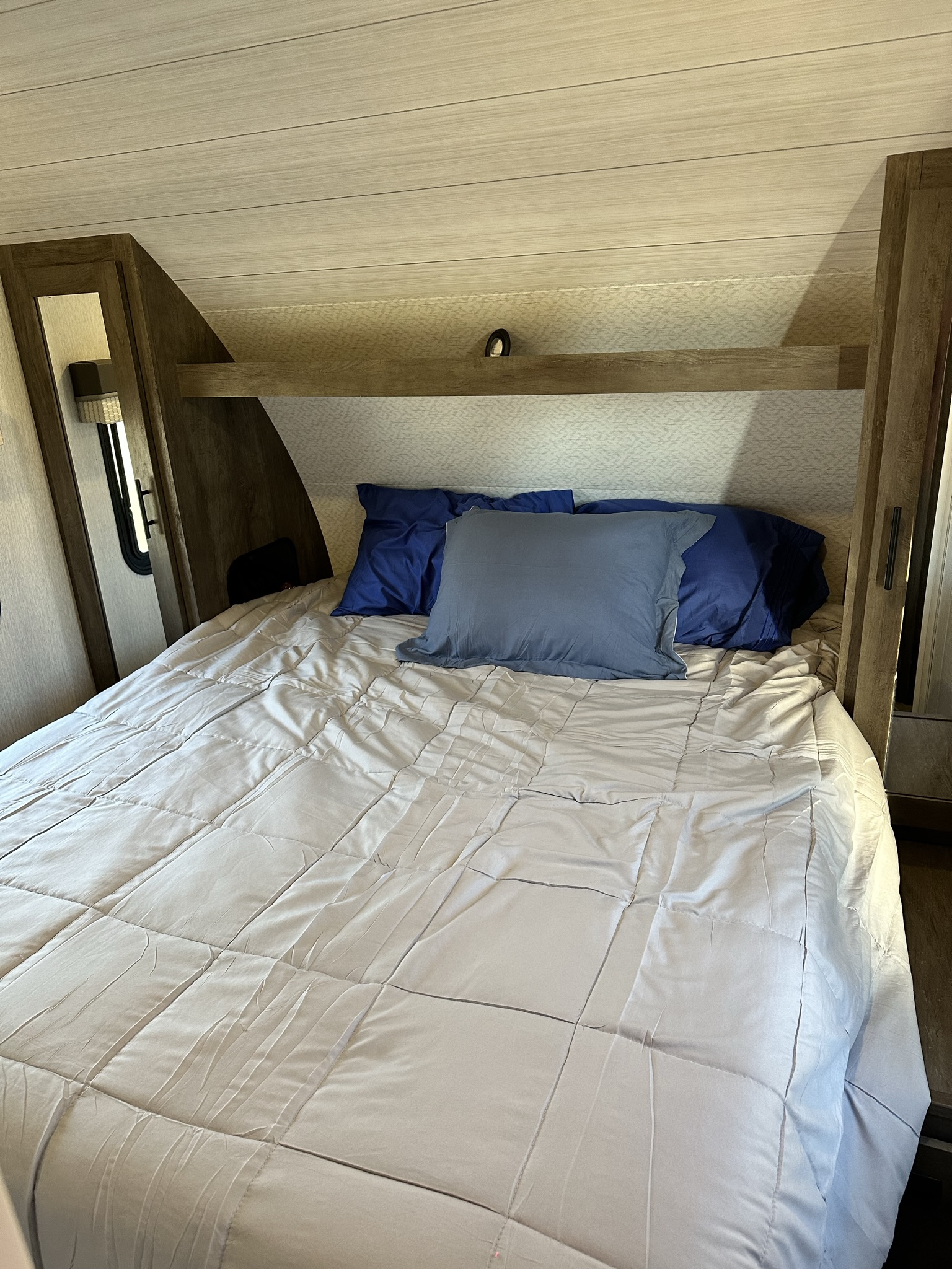 Cozy RV rental bedroom featuring a comfortable bed with blue pillows, built-in storage, and a warm ambiance.. Forest River Wildwood X-Lite 2022