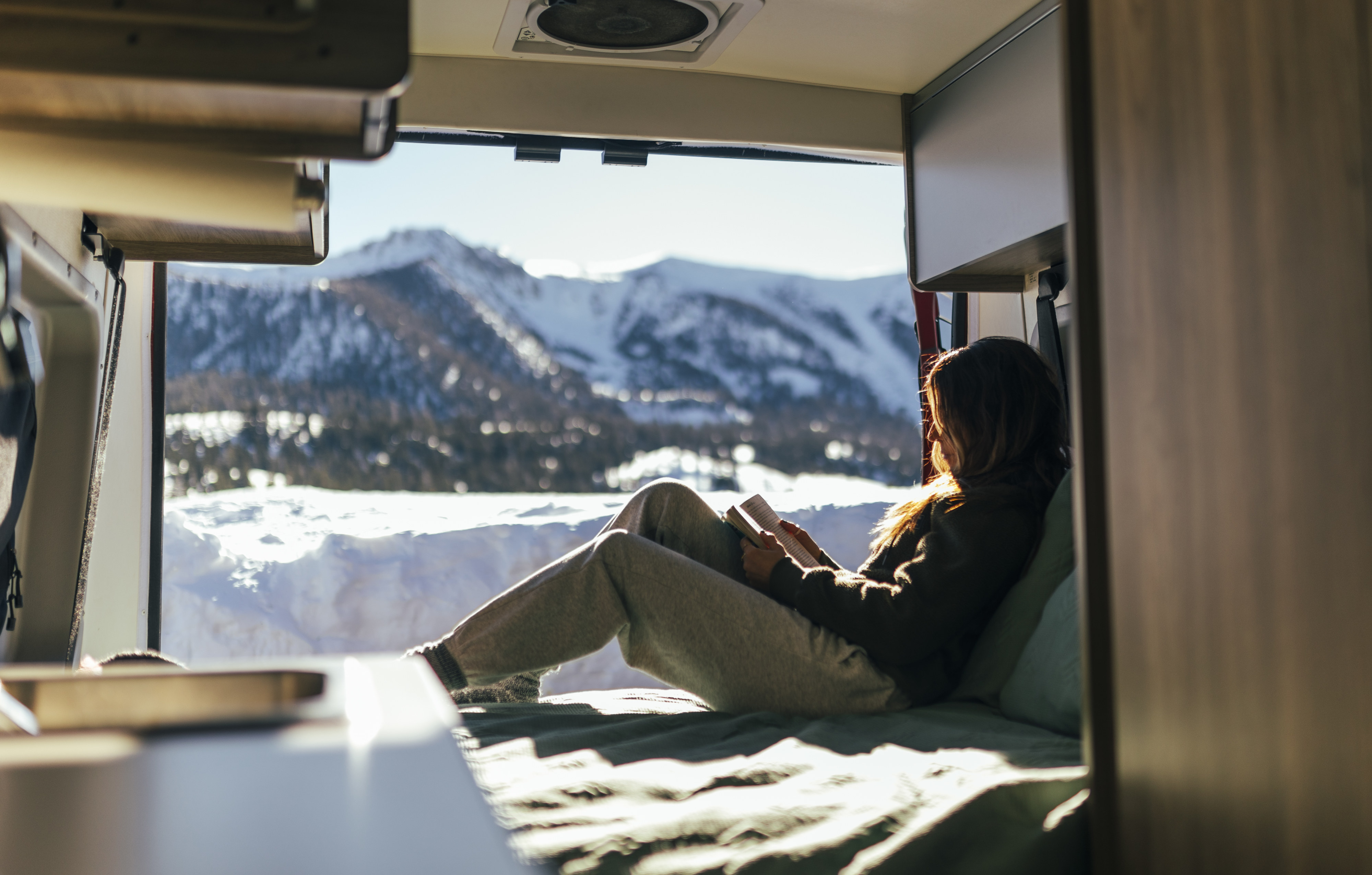 Woman relaxing inside an rv rental, reading a book with a stunning snowy mountain view from the back. Perfect winter escape.. Solis 59P Solis 2022