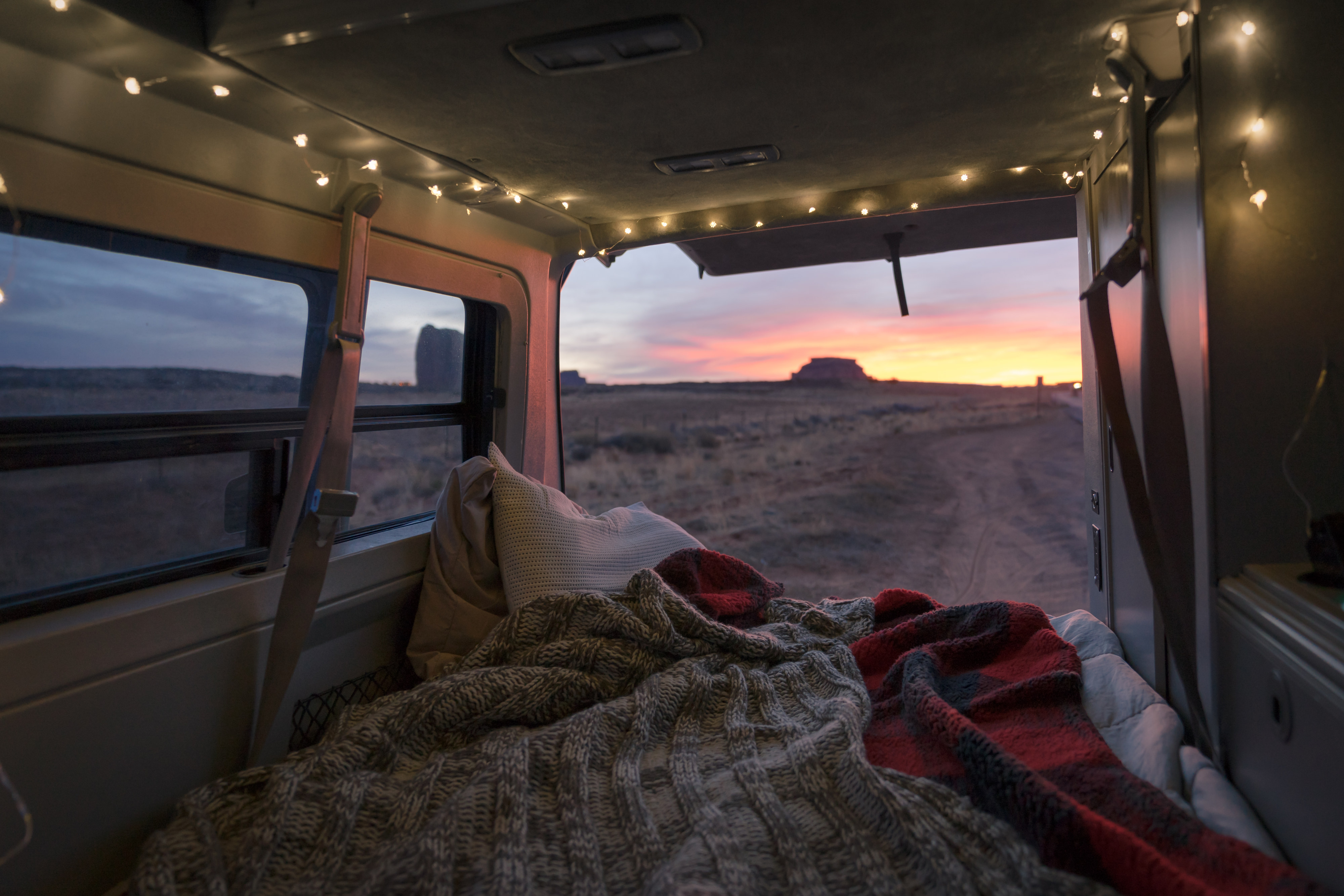 Experience cozy RV rental living: van interior with string lights, blankets, and a bed, overlooking a stunning desert sunset & rock formations.. Volkswagen Eurovan Full Camper 1999