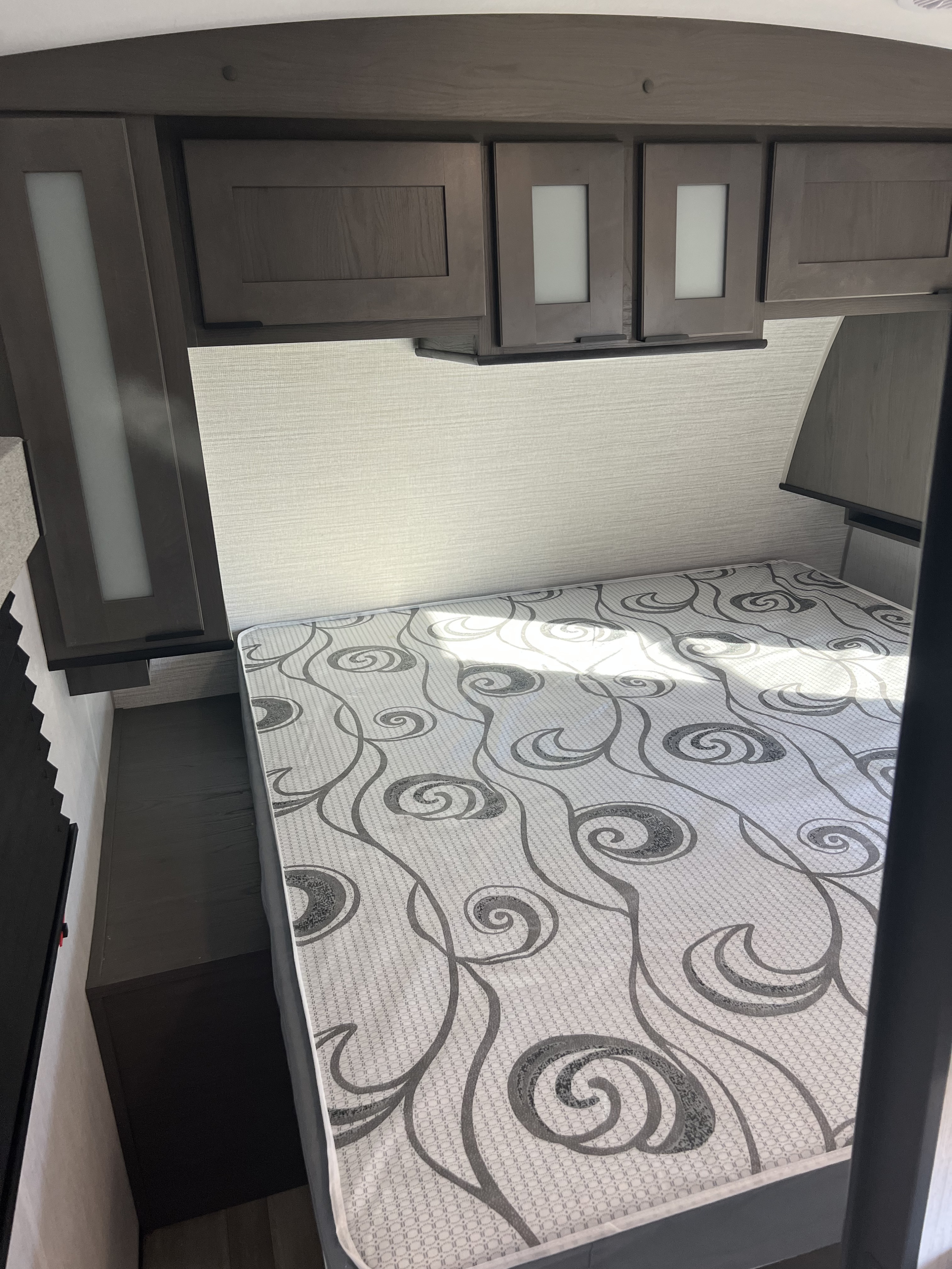 Cozy RV rental bedroom featuring a patterned mattress, dark wood overhead cabinets, and built-in bedside storage.. Cruiser RV MPG Ultra Lite 2022