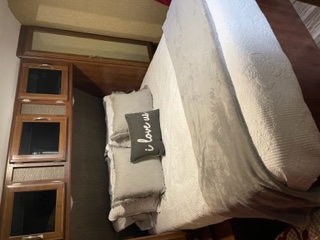 Comfortable RV bedroom featuring a queen bed with light bedding, a gray throw, and wooden built-in storage. Ideal for RV rental trips.. Keystone RV Passport Grand Touring 2017