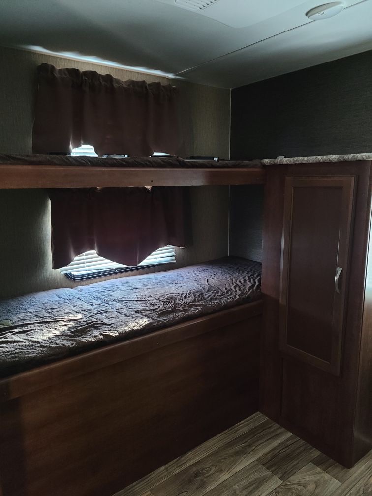 RV rental bunk bed sleeping area: Two bunks, curtained windows, and a cabinet. Practical and cozy RV interior.. Keystone RV Passport Grand Touring 2017