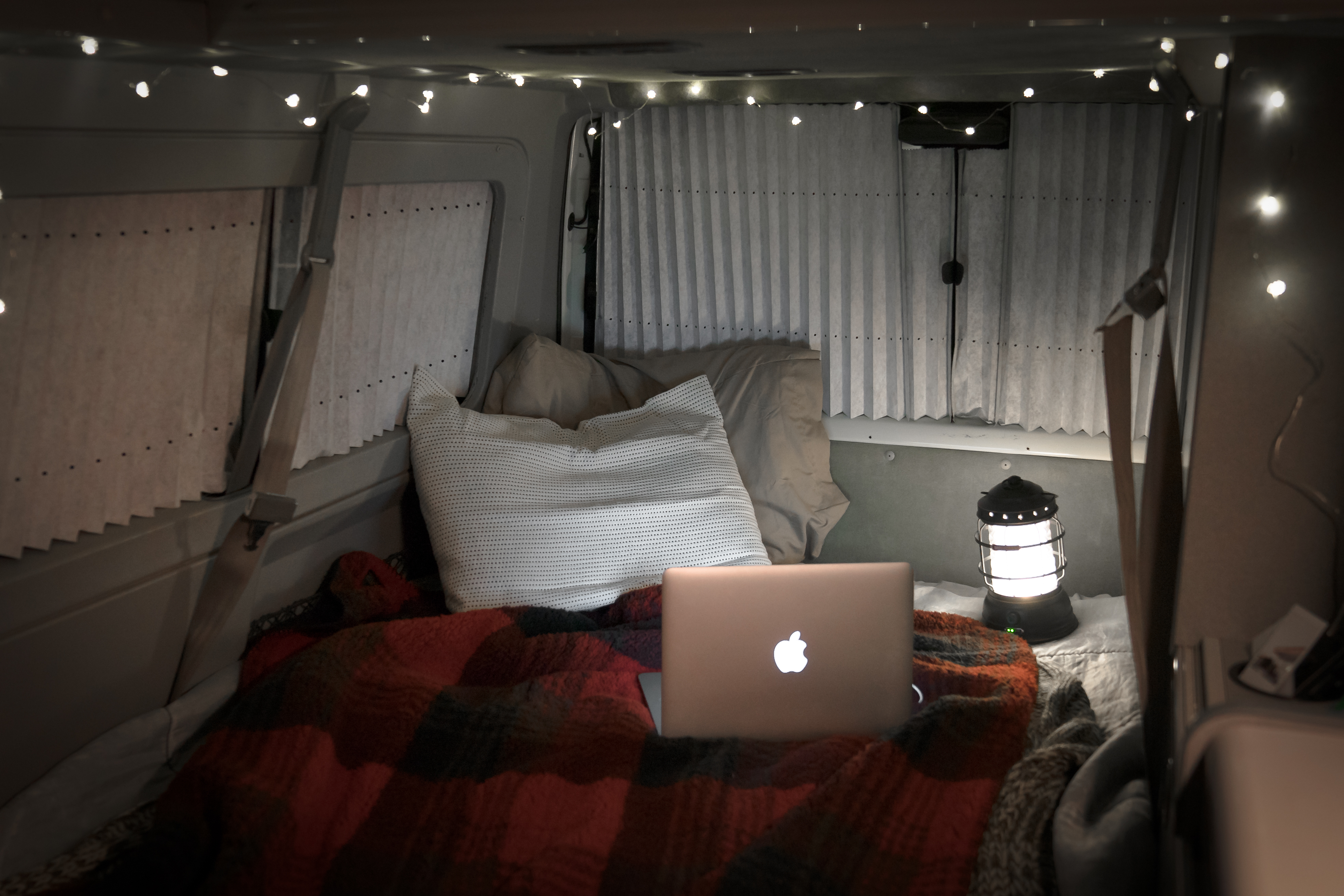 Cozy RV rental interior with a laptop on a bed, illuminated by a lantern and warm string lights, ideal for travel.. Volkswagen Eurovan Full Camper 1997