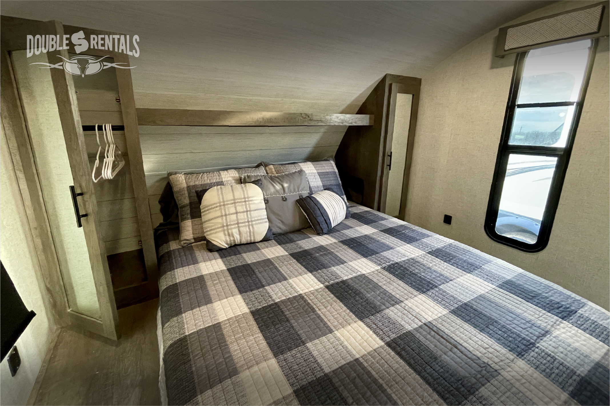 Inside a cozy RV rental bedroom featuring plaid bedding, a window, and built-in storage. Ideal for travelers.. Forest River Wildwood X-Lite 2020