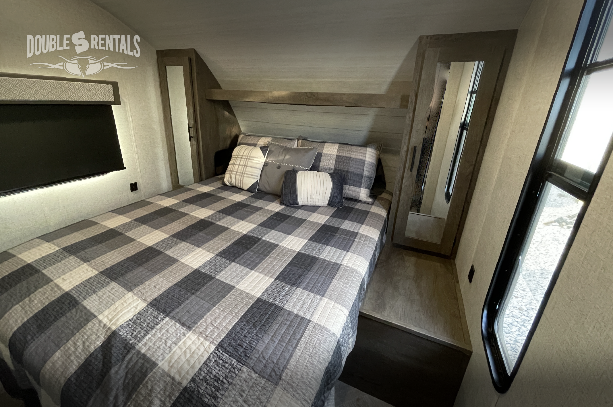 Cozy RV rental bedroom with comfortable plaid bed, overhead storage, and natural light from windows. Ideal for road trips.. Forest River Wildwood X-Lite 2020