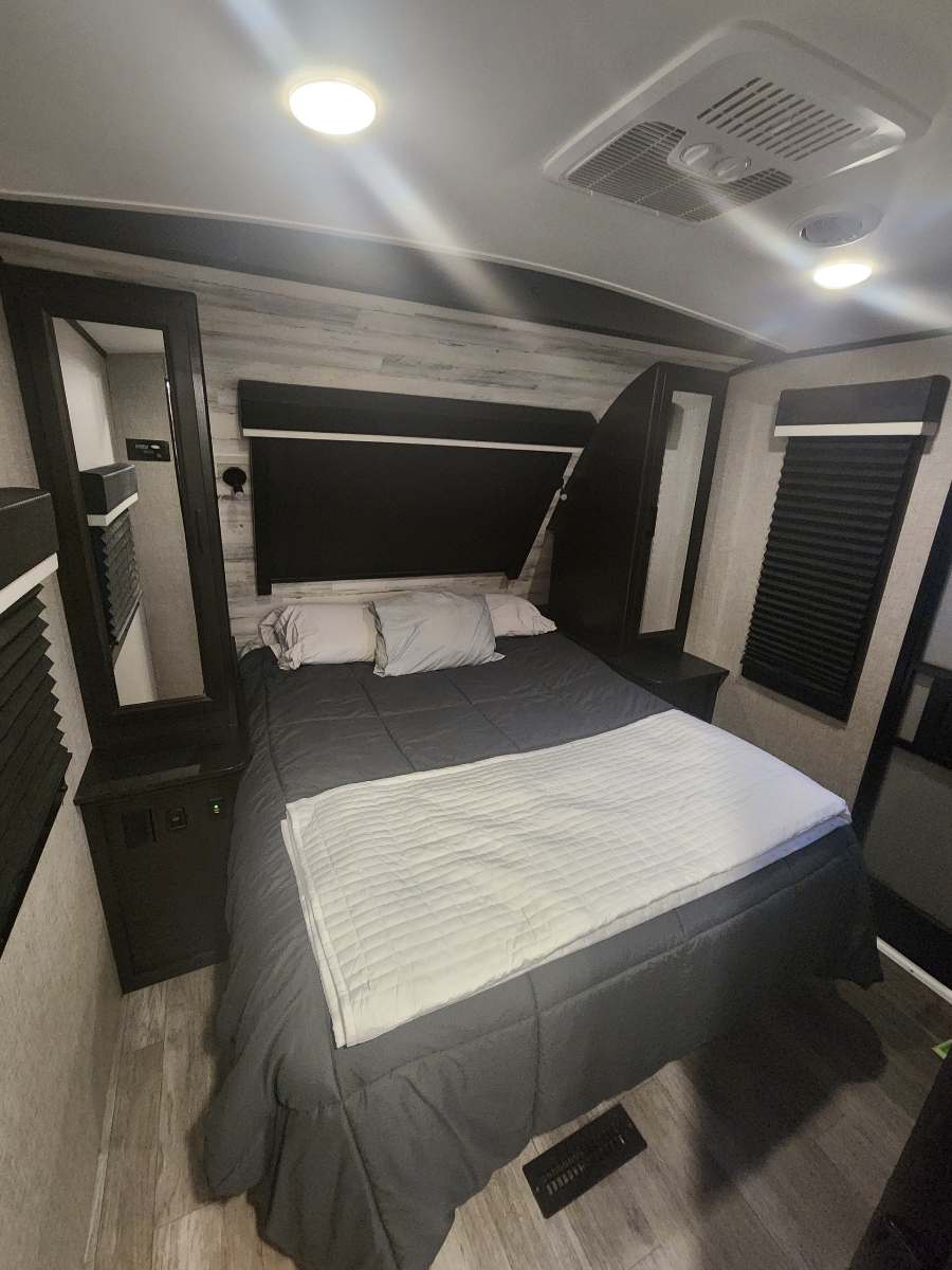 Cozy RV rental bedroom with a well-made bed, mirrored nightstands, and AC unit, offering a relaxing sleeping space.. Jayco White Hawk 2022