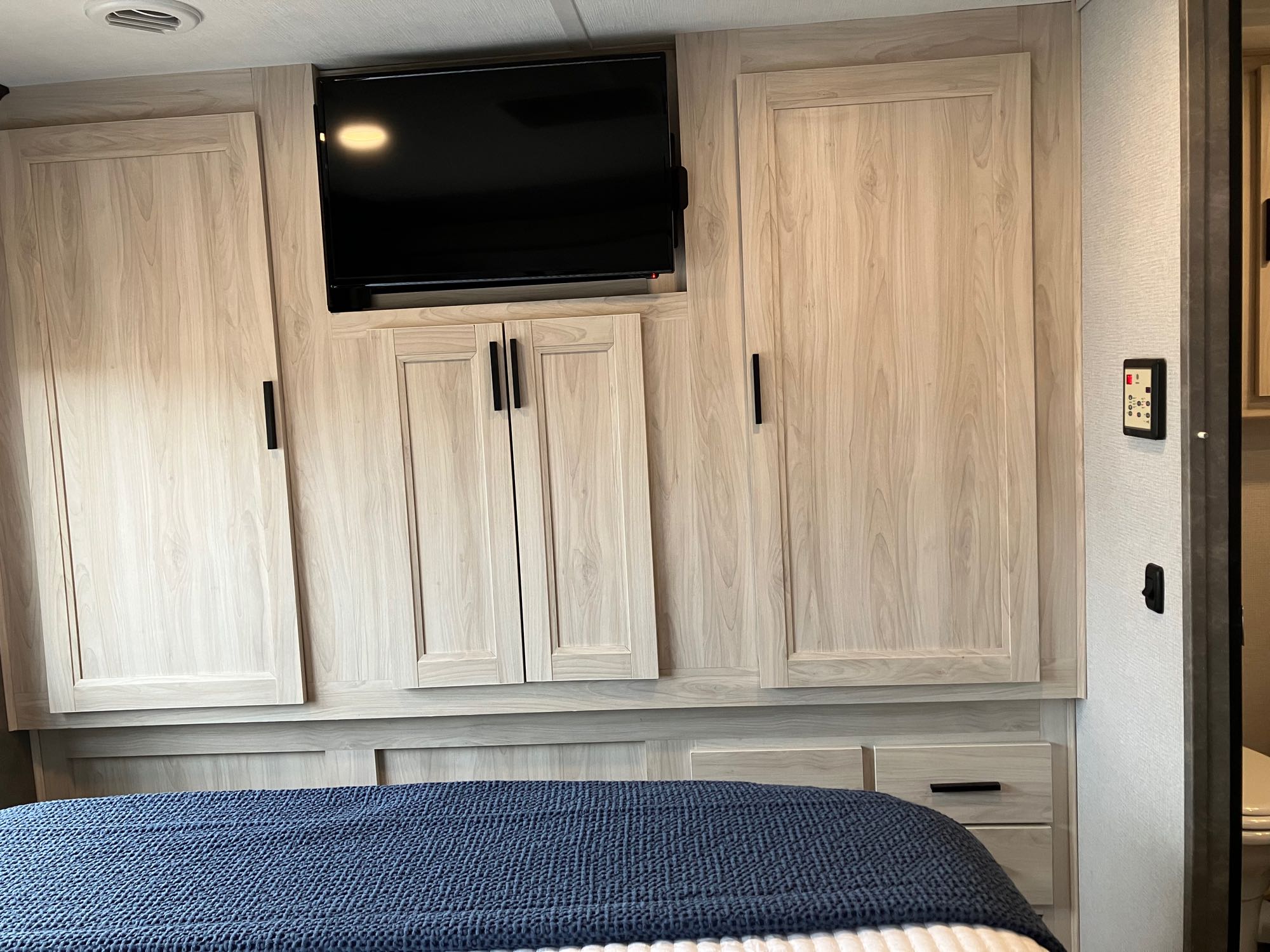 Cozy RV rental bedroom featuring light wood cabinets, a wall-mounted TV, and an illuminated control panel on the right.. Forest River Sunseeker 2020