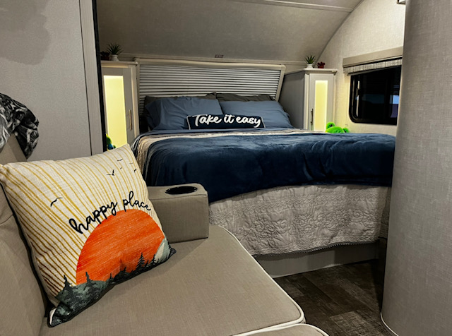Inviting RV rental bedroom with a comfy blue bed, glowing side cabinets, and "happy place" couch pillow.. Forest River RPod Hood River Addition 2022