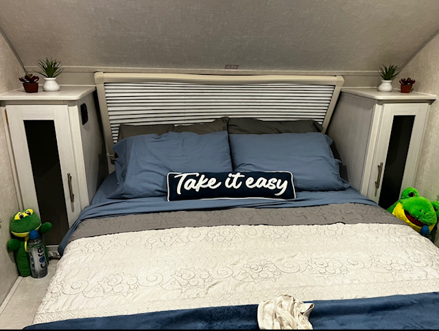 Inside a cozy RV rental bedroom: blue bedding, 'Take it easy' pillow, built-in storage, and two stuffed frogs.. Forest River RPod Hood River Addition 2022