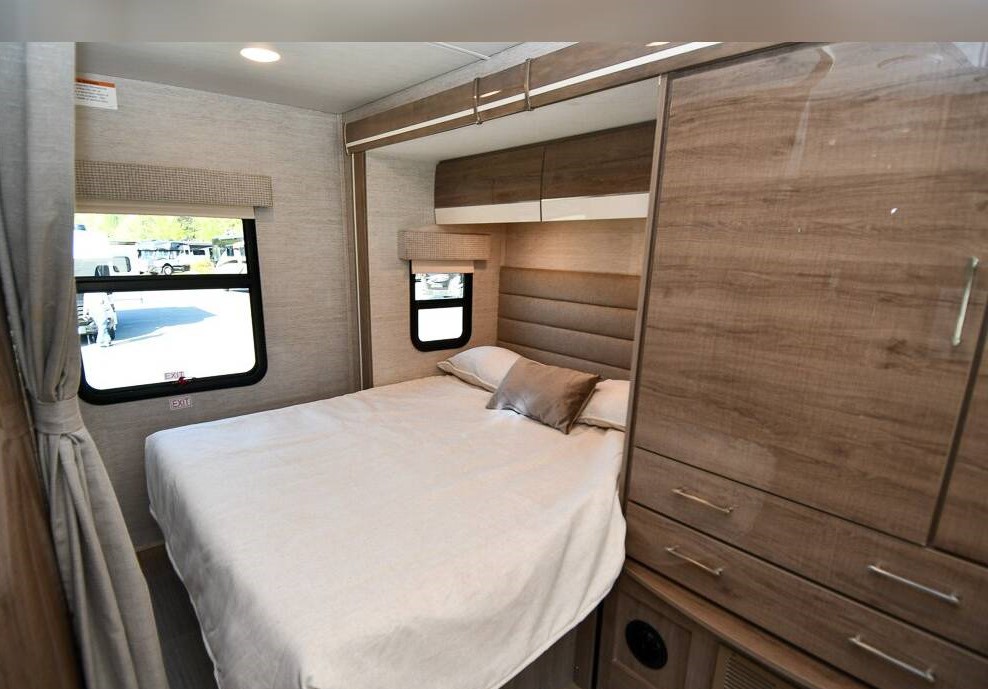 Bright RV rental bedroom with a neatly made bed, padded headboard, overhead cabinets, and a tall wardrobe unit.. Jayco Melbourne 2023