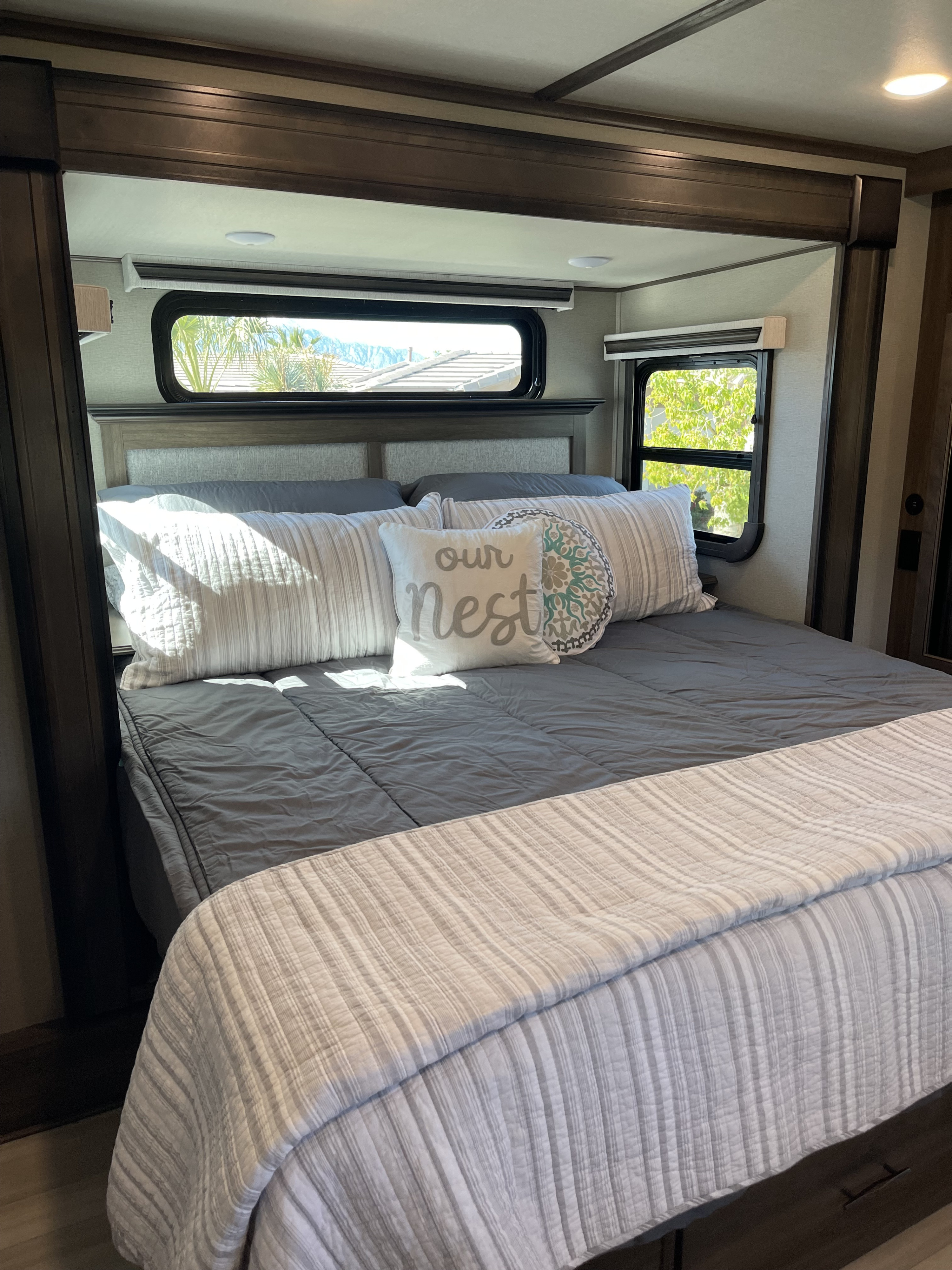 Comfortable RV rental bedroom showcasing a queen bed, decorative pillows, and scenic windows for a relaxing retreat.. Grand Design Solitude 2022