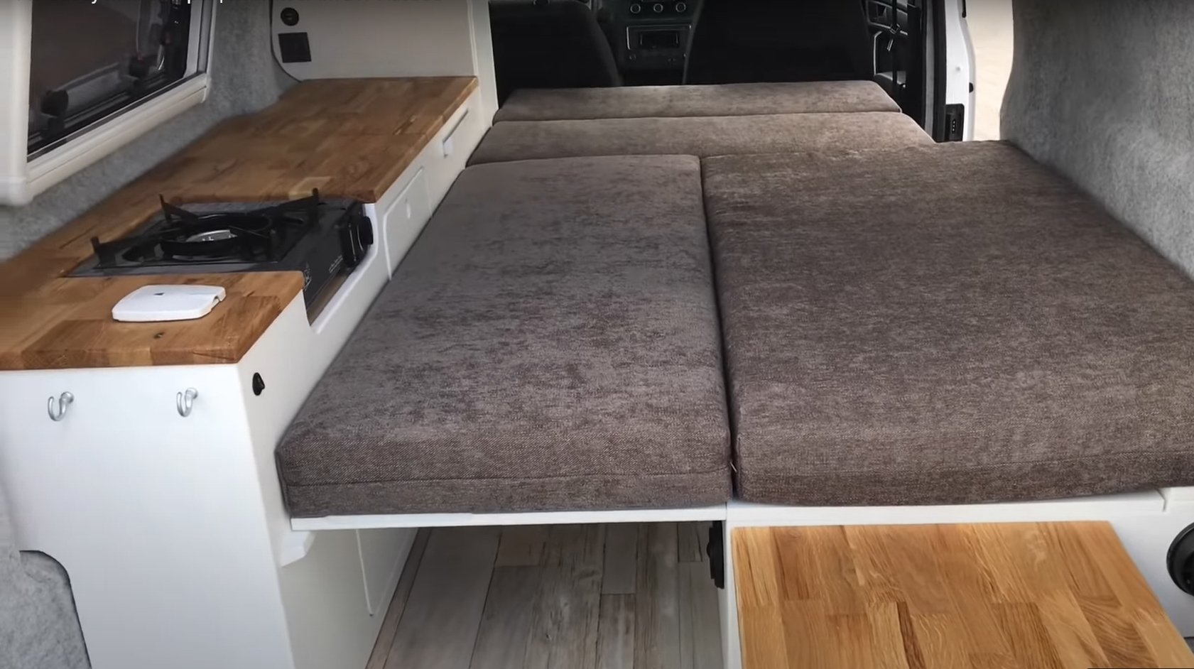 RV rental camper van interior: features a compact kitchen with wood counter & stove, alongside a versatile bed area.. volkswagen Caddy 2010