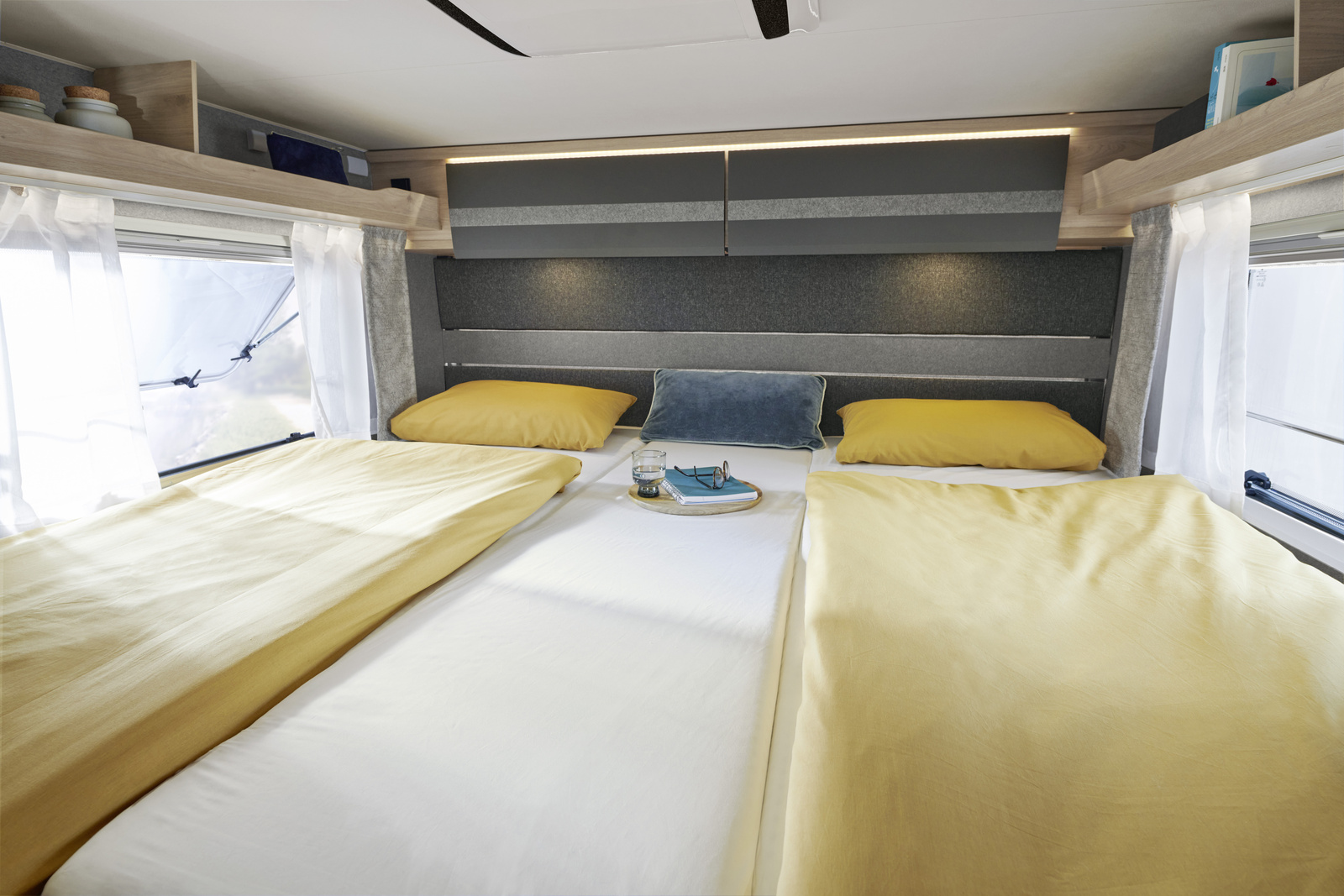 Cozy RV rental bedroom with two single beds, yellow bedding, overhead storage, and natural light from windows.. Dethleffs Dethleffs Just 6812 2023