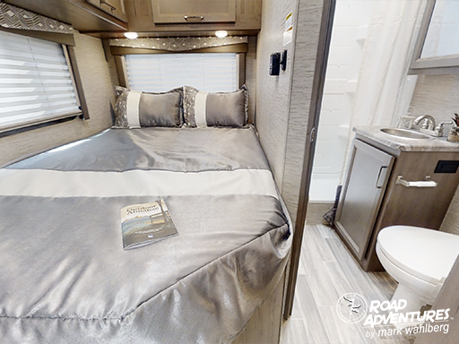 Inside an RV rental, showing a comfortable bedroom area with a bed and adjacent compact bathroom featuring a toilet and sink.. Thor Motor Coach Four Winds 22E 2024