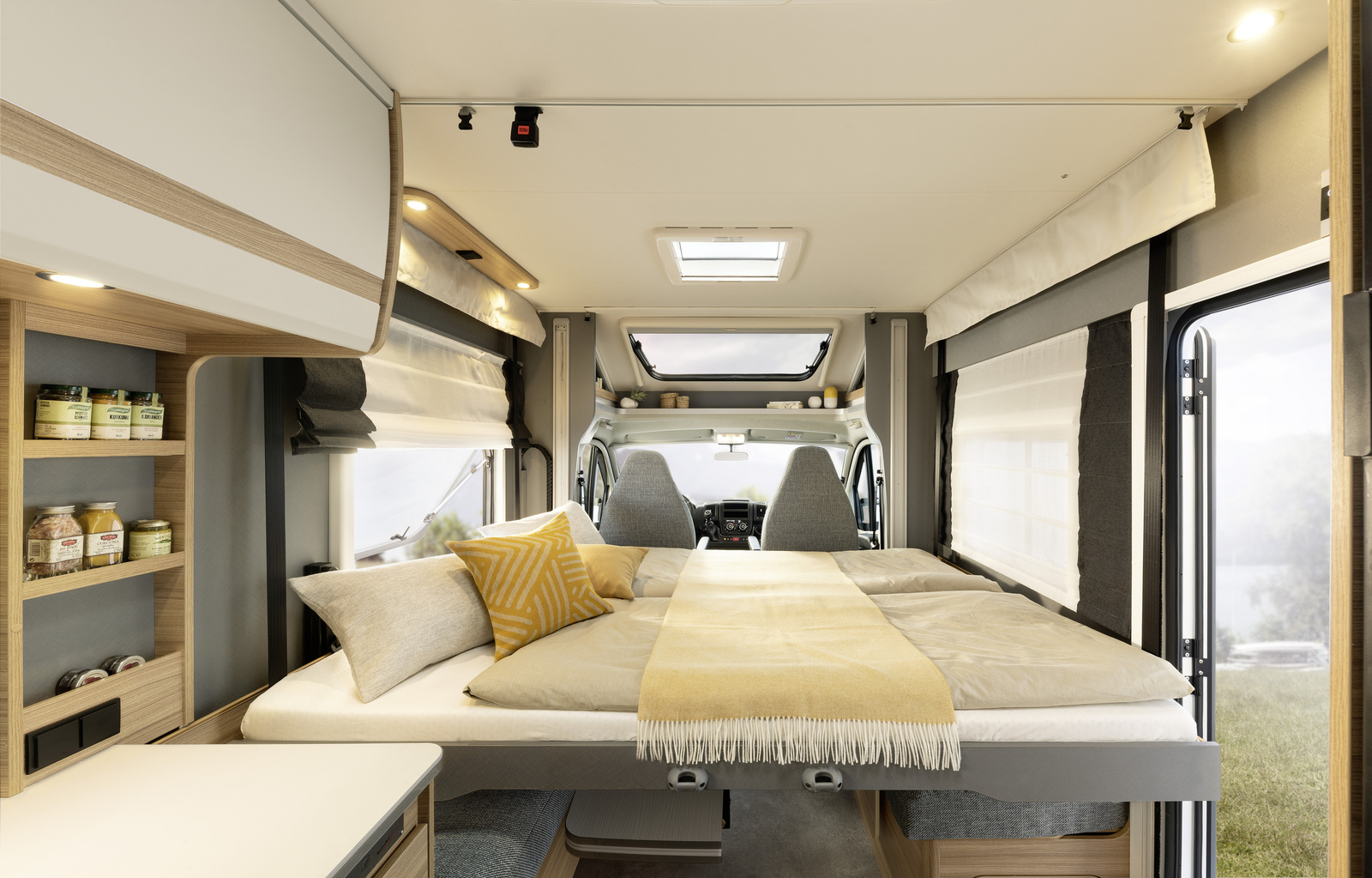 Comfortable RV rental interior: a spacious bed, shelving with jars, and bright light from side windows overlooking nature.. Dethleffs JUST T7052 DBM 2023