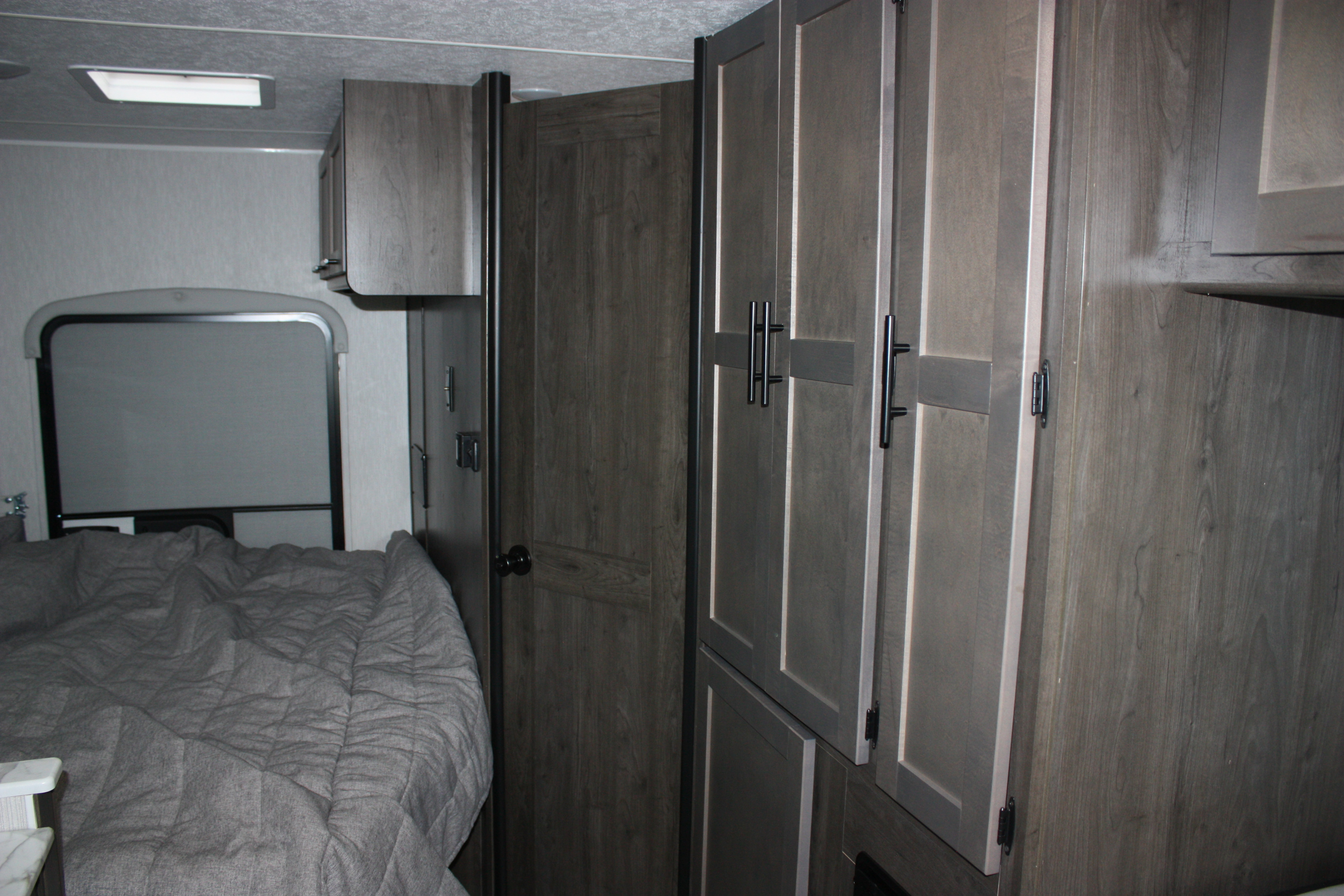 View of an RV rental bedroom with a gray bed, window, and modern wood storage cabinets. Compact living space.. Coachmen Cross Trail 21XG 2022