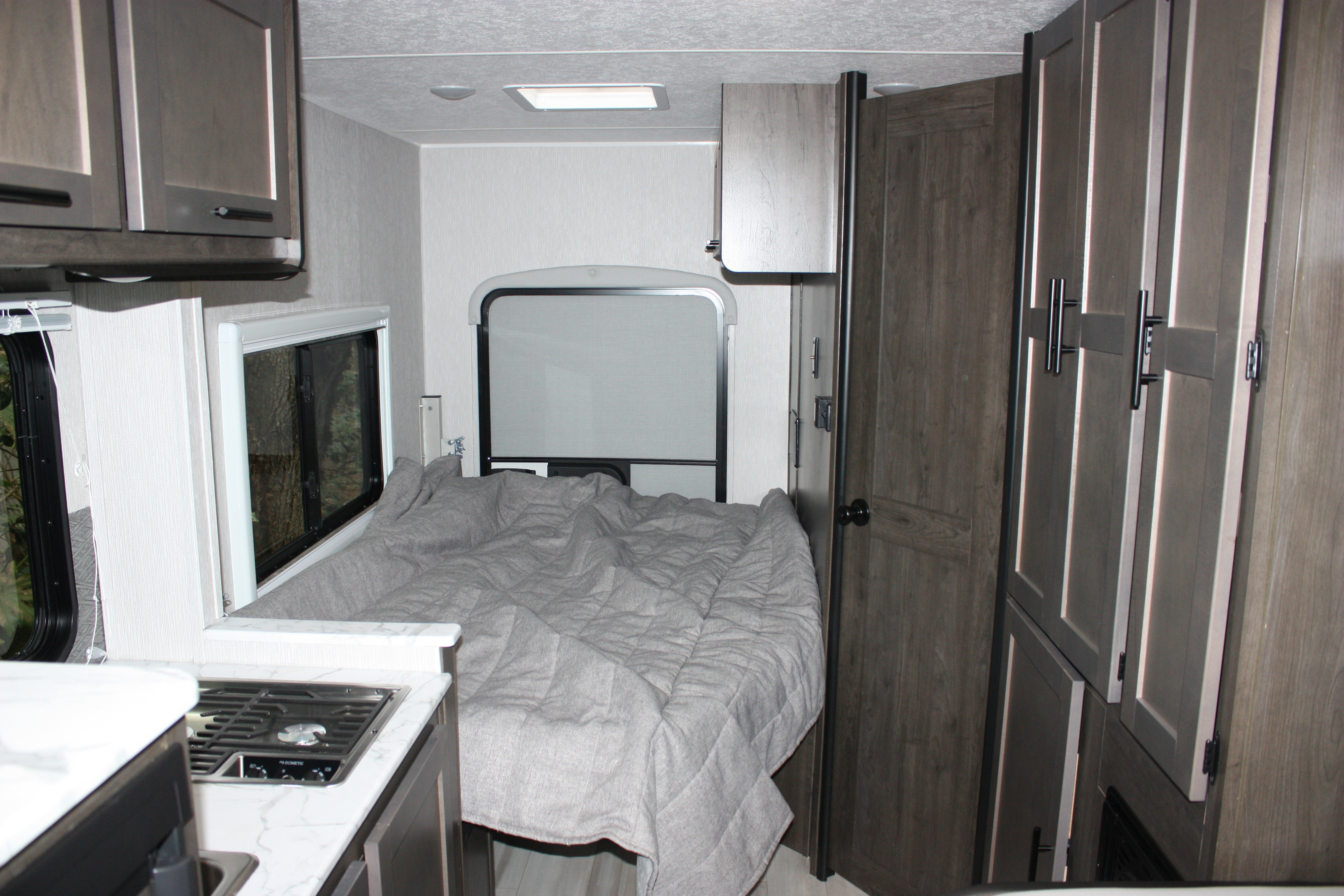 RV rental interior showing a compact kitchen with a stovetop and a comfortable bed with a gray blanket.. Coachmen Cross Trail 21XG 2022