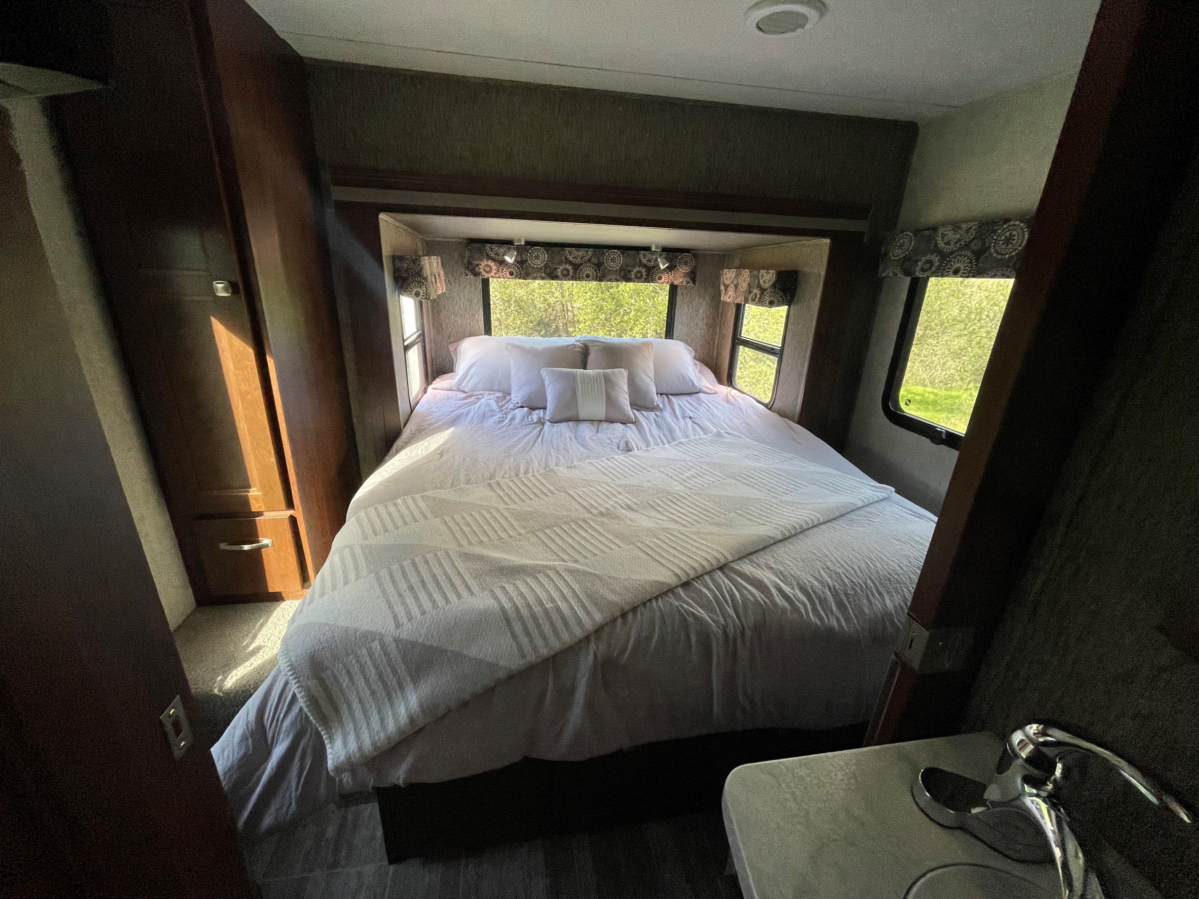 This RV rental interior features a comfortable bedroom with a large bed, crisp white bedding, and bright nature views from side windows.. Forest River Sunseeker MBS 2018