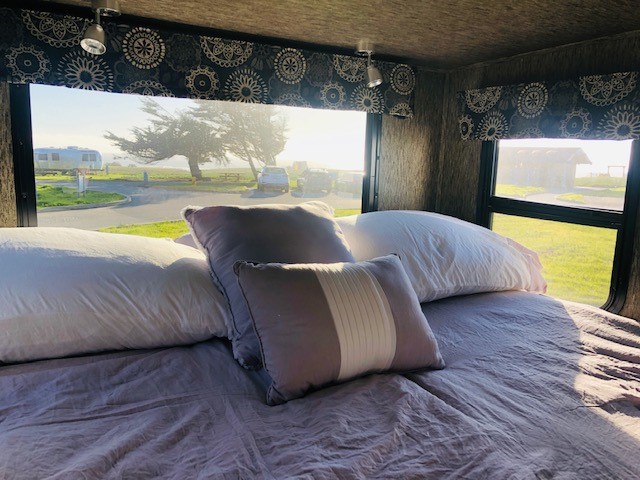 Cozy RV rental bedroom with plush bed and pillows, showcasing a bright coastal campground view with an Airstream.. Forest River Sunseeker MBS 2018