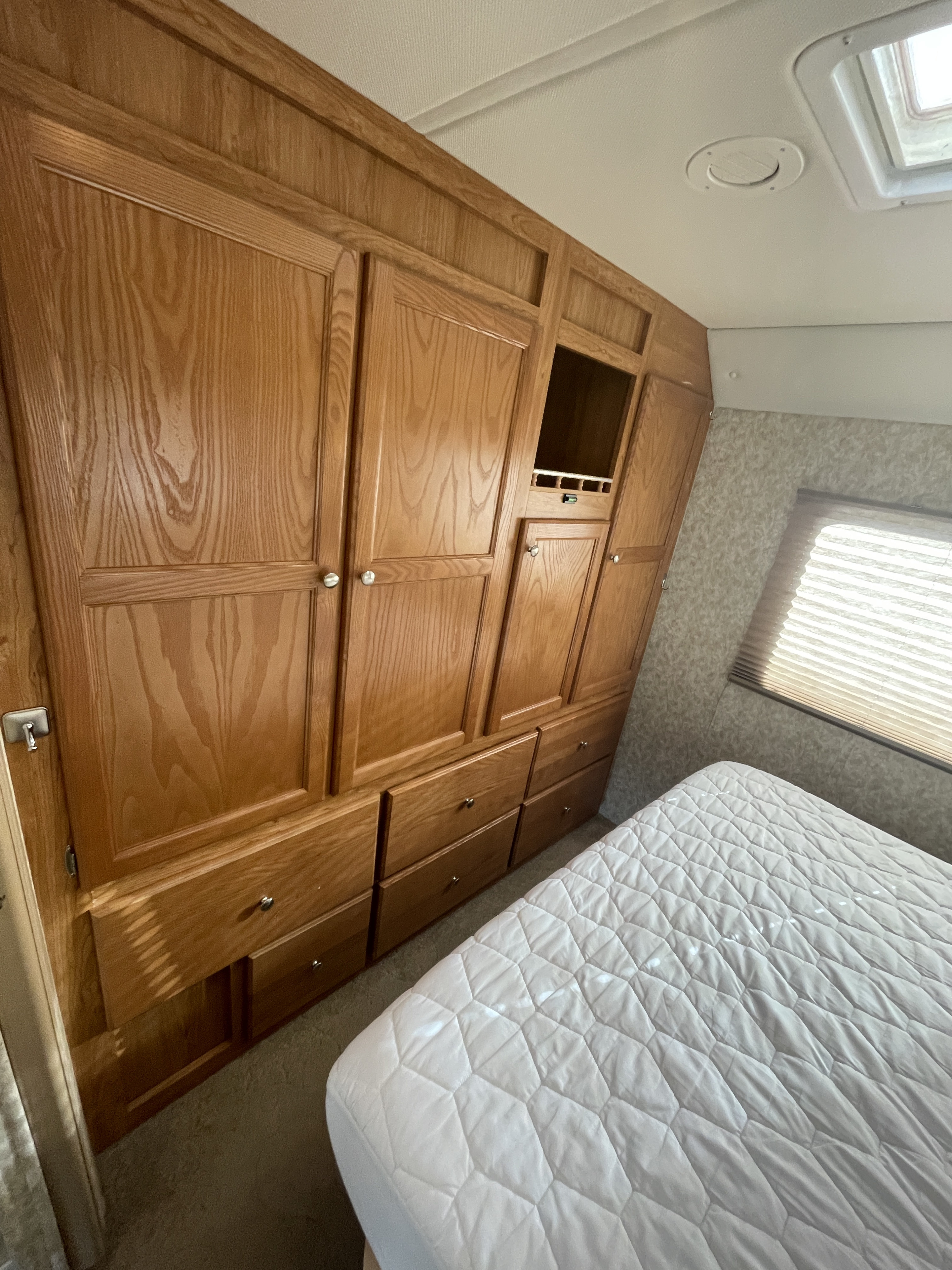 Bedroom interior of an rv rental, featuring a quilted bed, wood cabinets, & ample storage solutions for travel.. Safari Ivory 2006