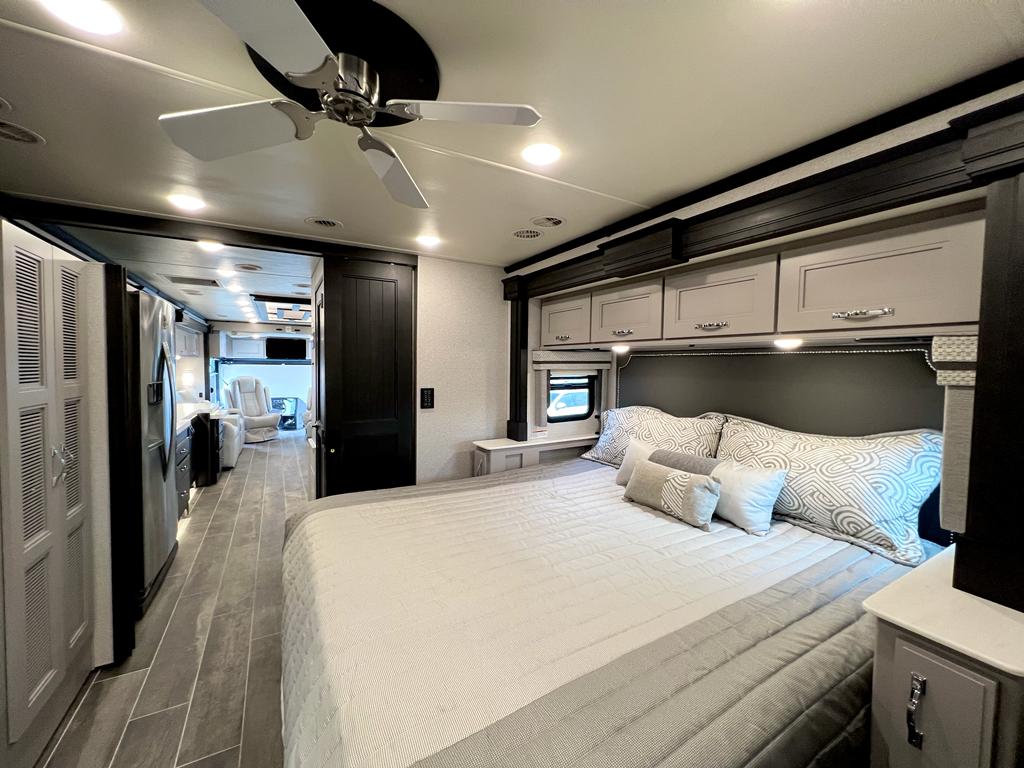 Luxurious RV rental bedroom features a comfortable queen bed, ceiling fan, and overhead storage, opening to the living area. Ideal for travel.. Thor Motor Coach Venetian 2023