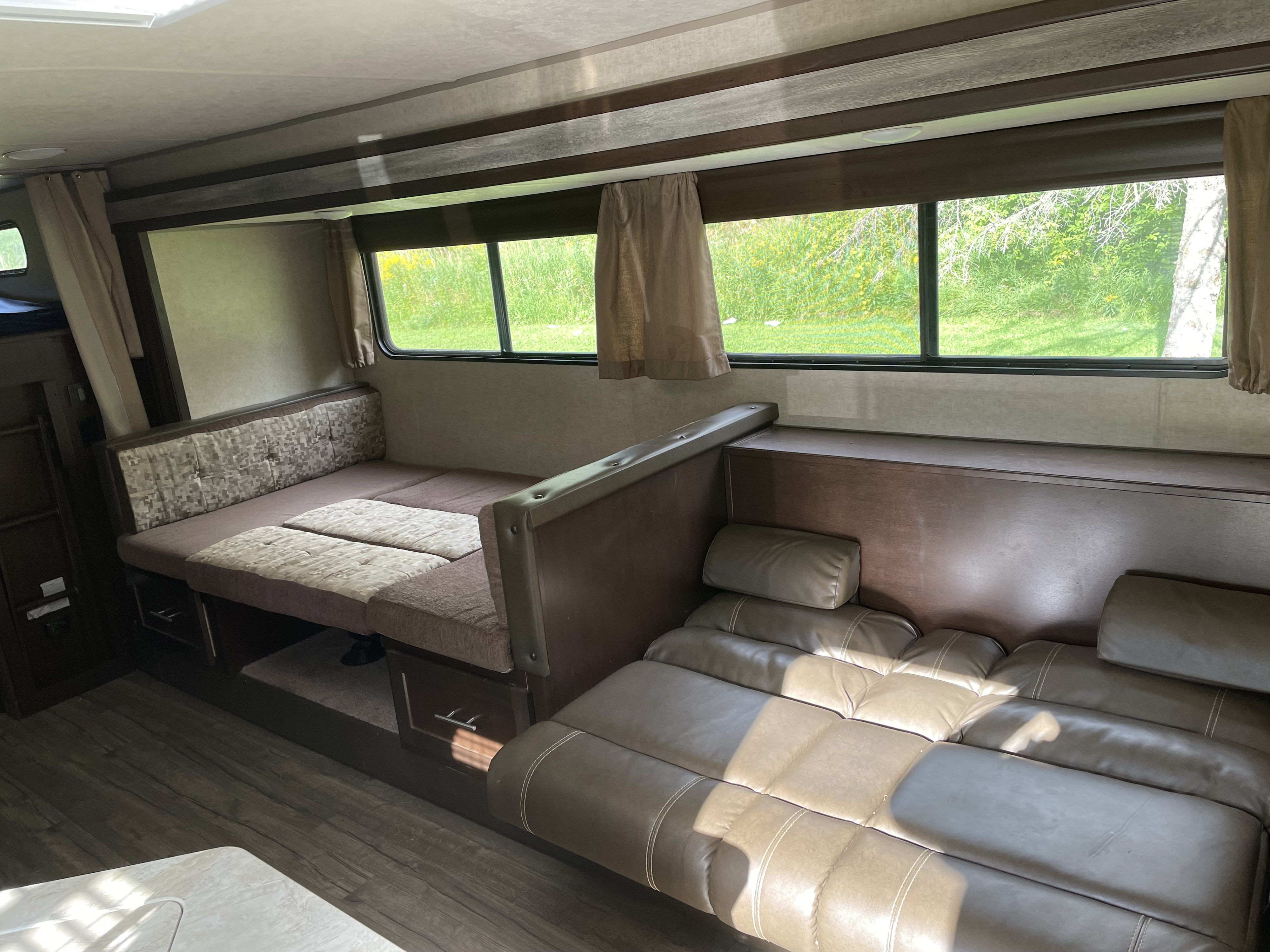 Spacious RV rental interior with a cozy dinette, comfortable sofa, and large windows revealing a lush green outdoor view.. Forest River Cherokee Grey Wolf 2017