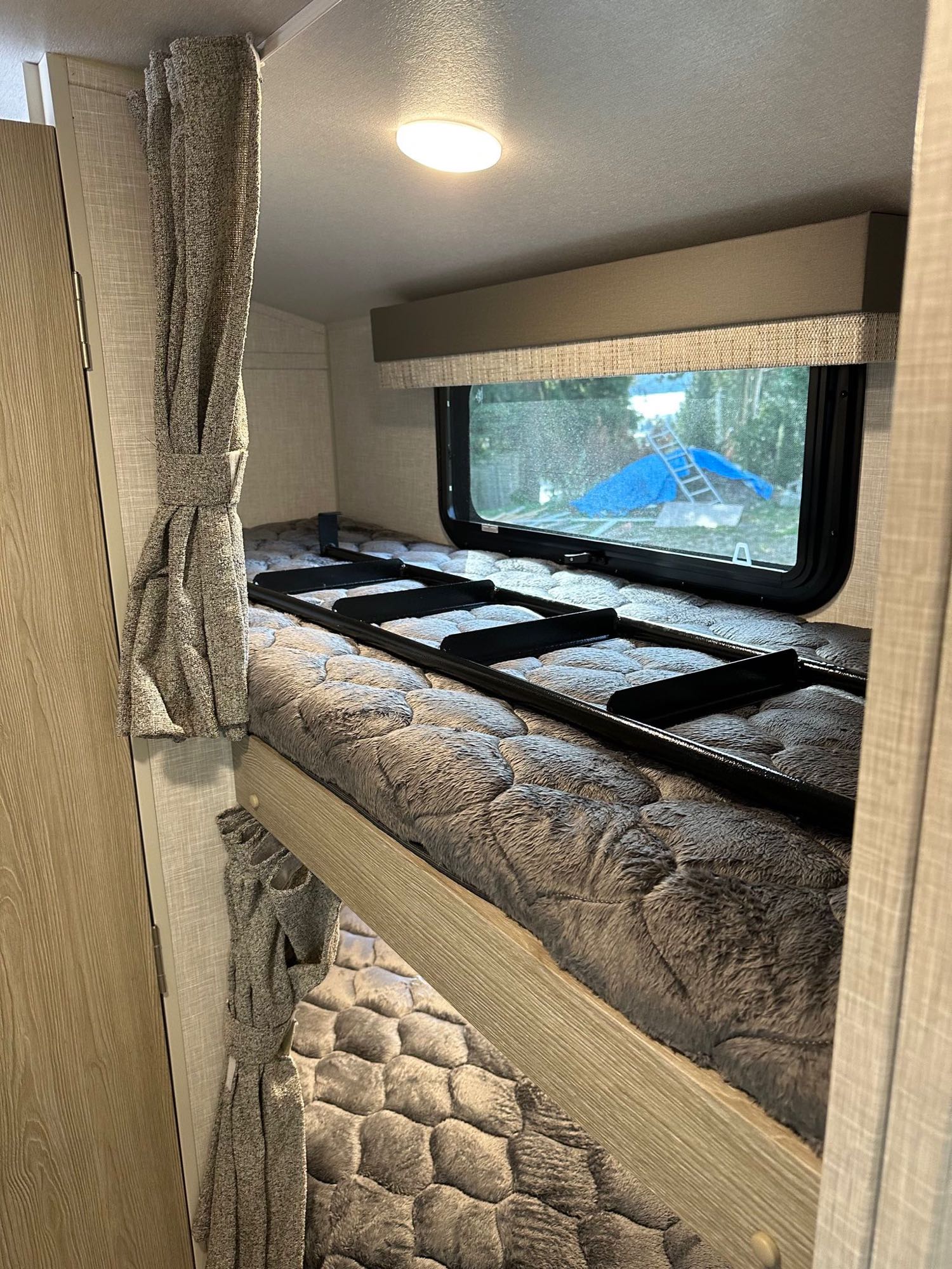 Experience comfort in this RV rental's bunk bed area, featuring cozy grey bedding, window, and ladder.. Forest River Flagstaff E-Pro 2022