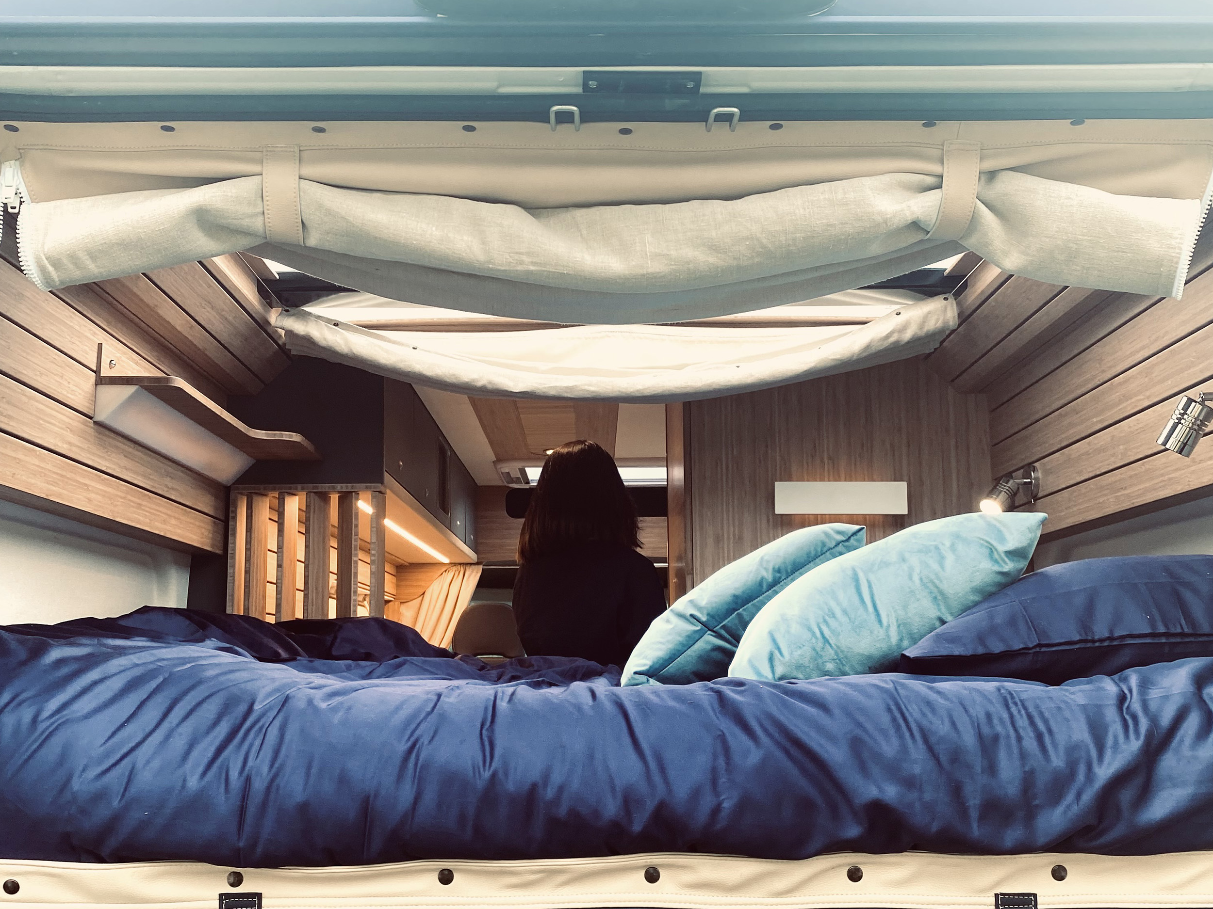 Inside a modern RV rental: a comfortable bed with blue bedding, warm wooden finishes, and soft lighting.. Fiat Ducato 2021