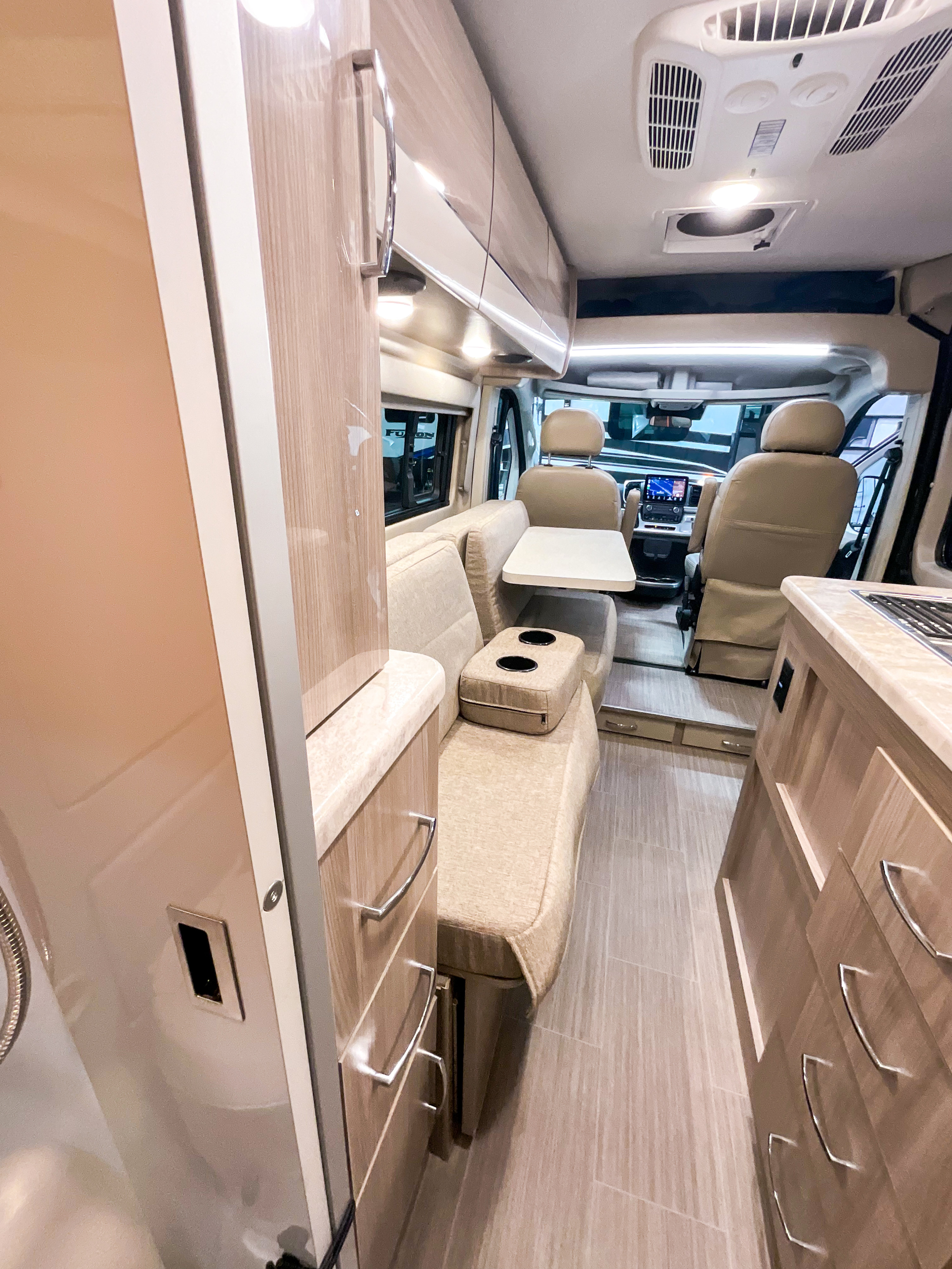 Inside a modern **rv rental**: light-toned interior with a cozy living area, dining table, kitchen counter, and front cab.. Dodge Ram Thor scope 2023